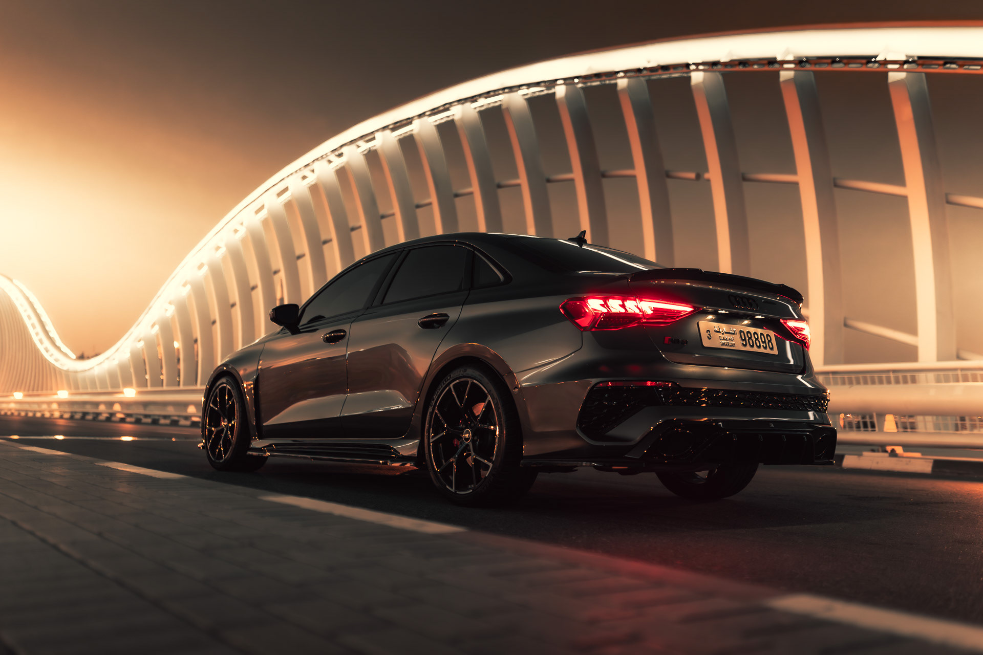 Audi RS3 2023 on Dubai bridge at night with glowing white light arcs and warm reflections
