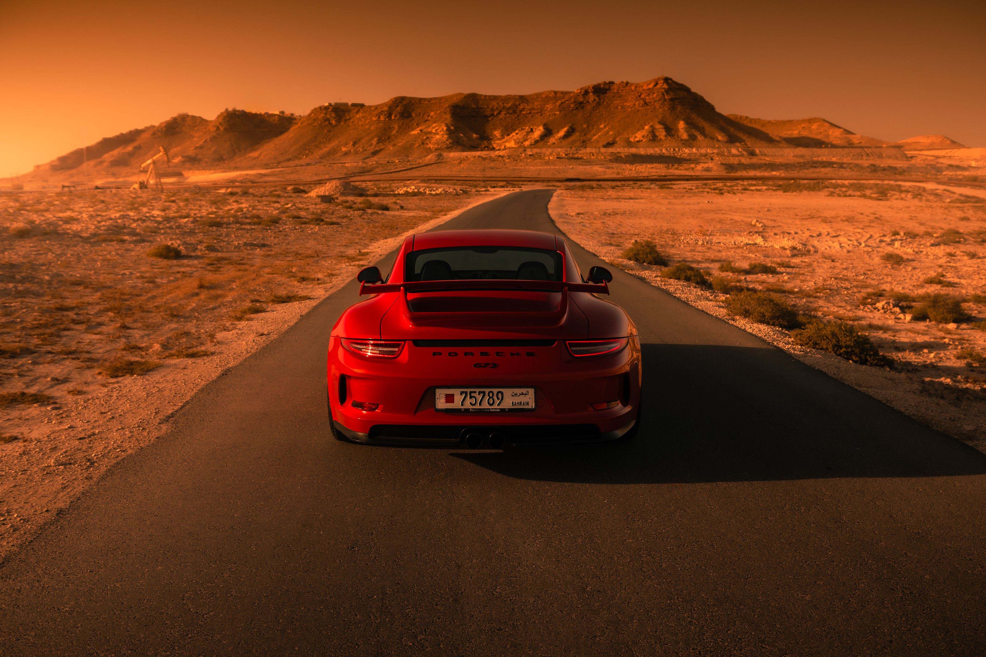Rear view of Porsche 911 GT3 on the road, sunset mountains and winding desert path ahead.