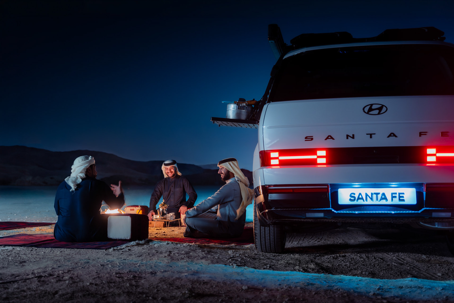 HYUNDAI SANTA FE illuminated rear badge and taillights at night with the group seated by the fire, Bahrain — Shift Mootark