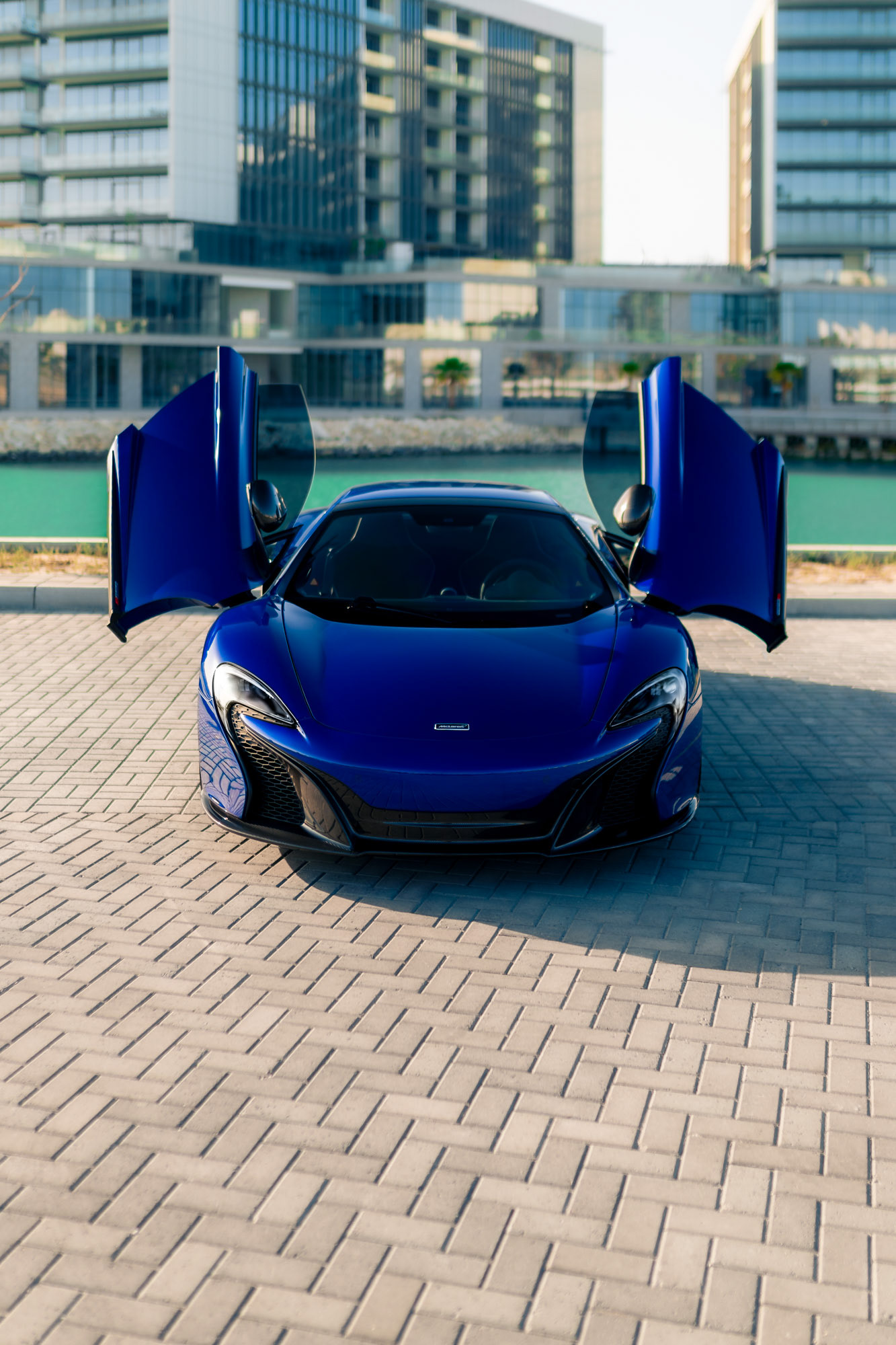 Front view of the McLaren 650S Spider in Bahrain with dihedral doors open, captured in daylight against modern waterfront architecture