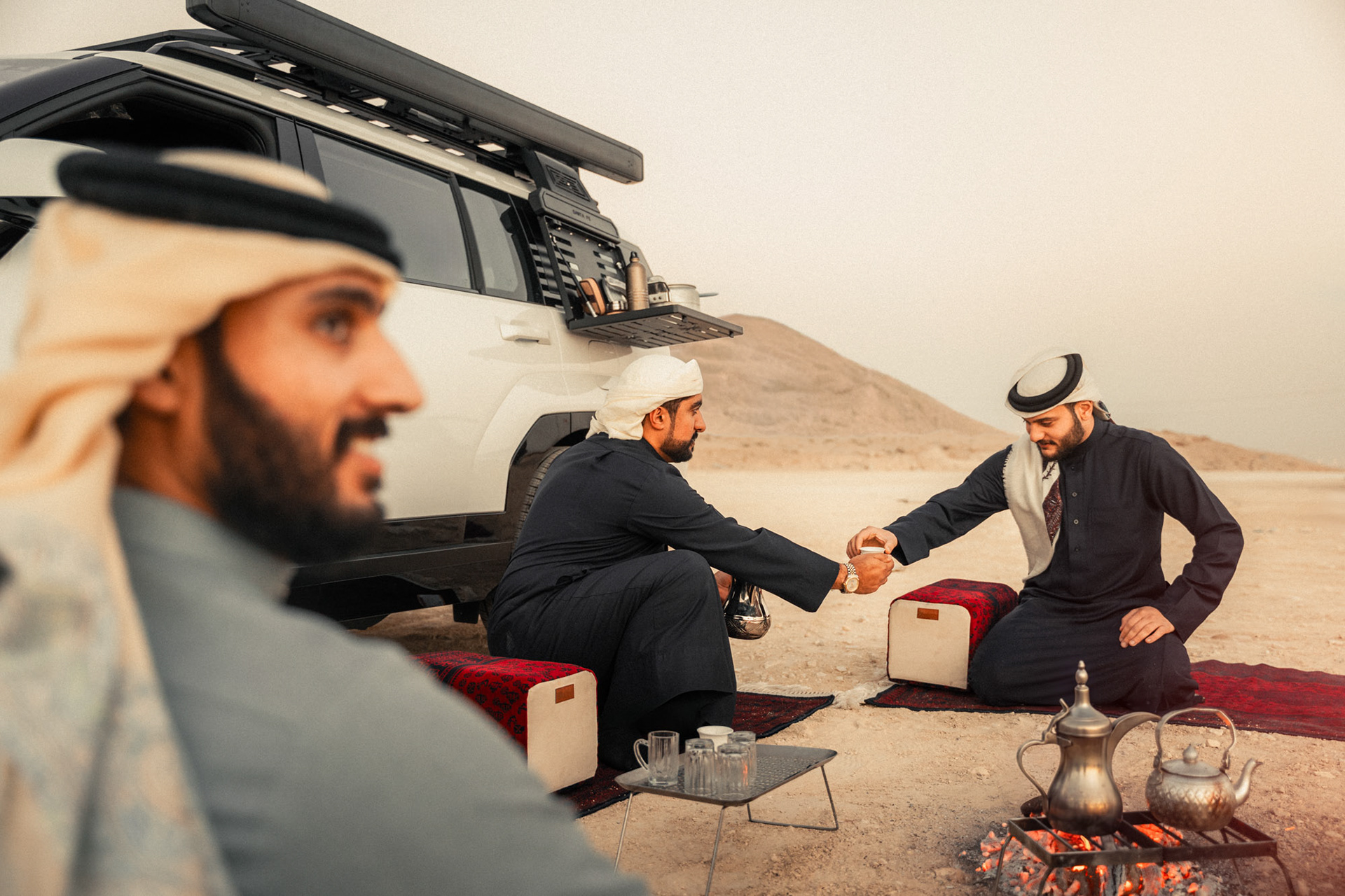 HYUNDAI SANTA FE road trip group pouring Arabic coffee and tea by the fire at dusk, Bahrain — Shift Mootark