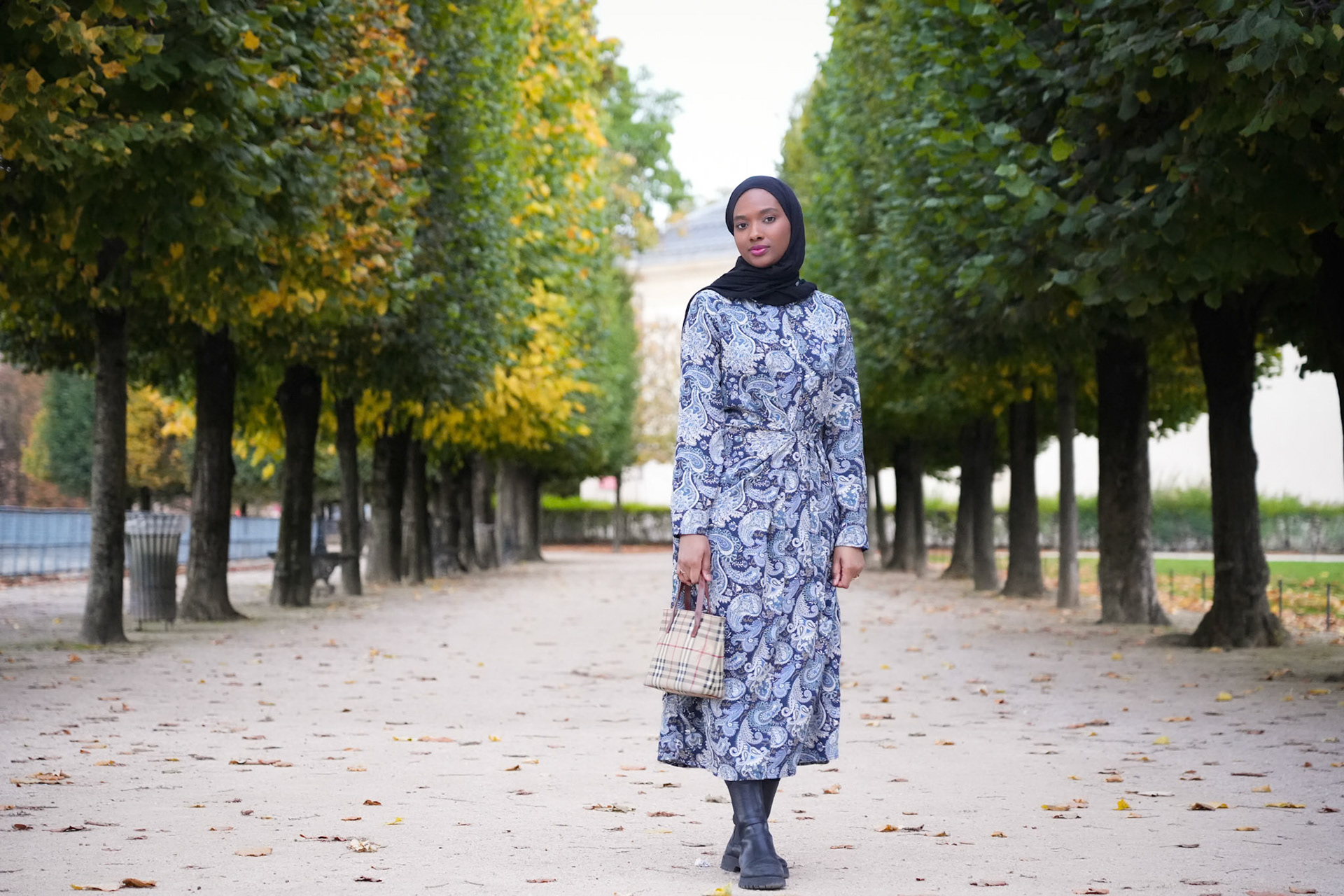 A black muslim girl stands in front of trees with different colours at the Tuileries garden (Jardin des Tuileries) in an autumn afternoon.