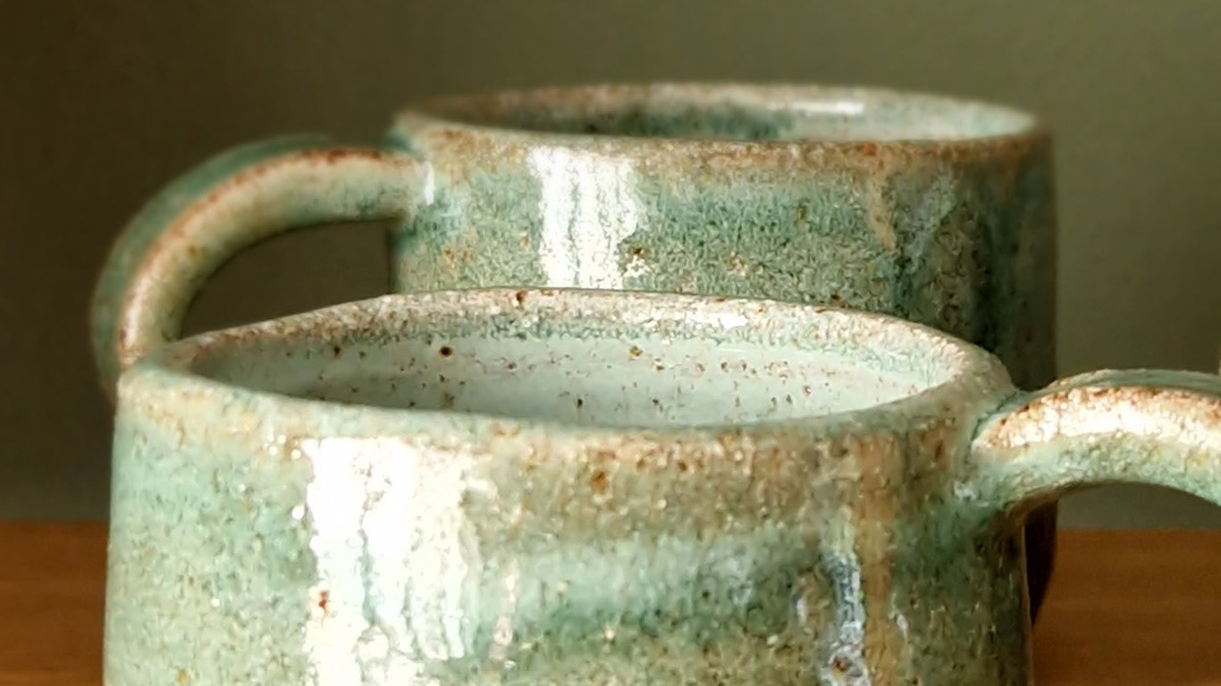 A close-up photograph of two green ceramic mugs flecked with brown.