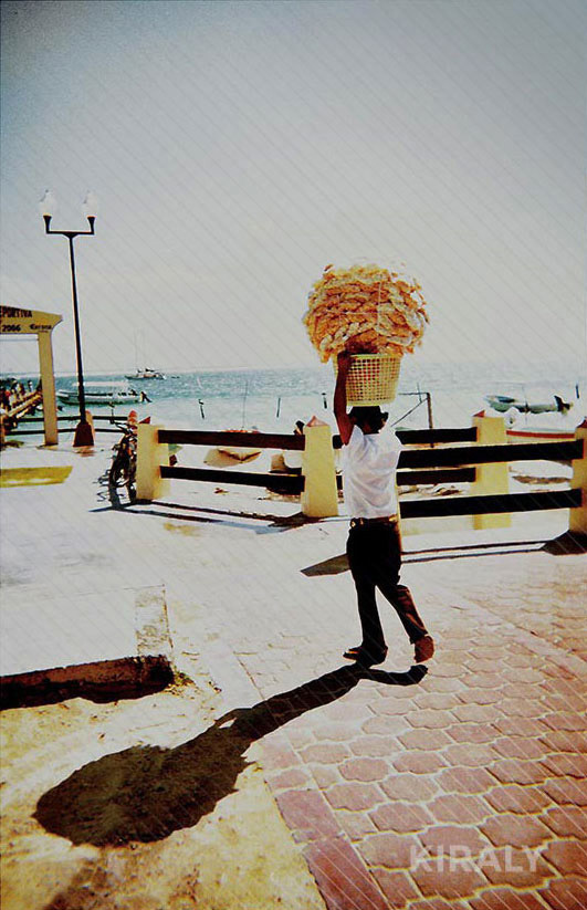 Person walking with a basket of supplies on top of his head casting an interesting shadow
