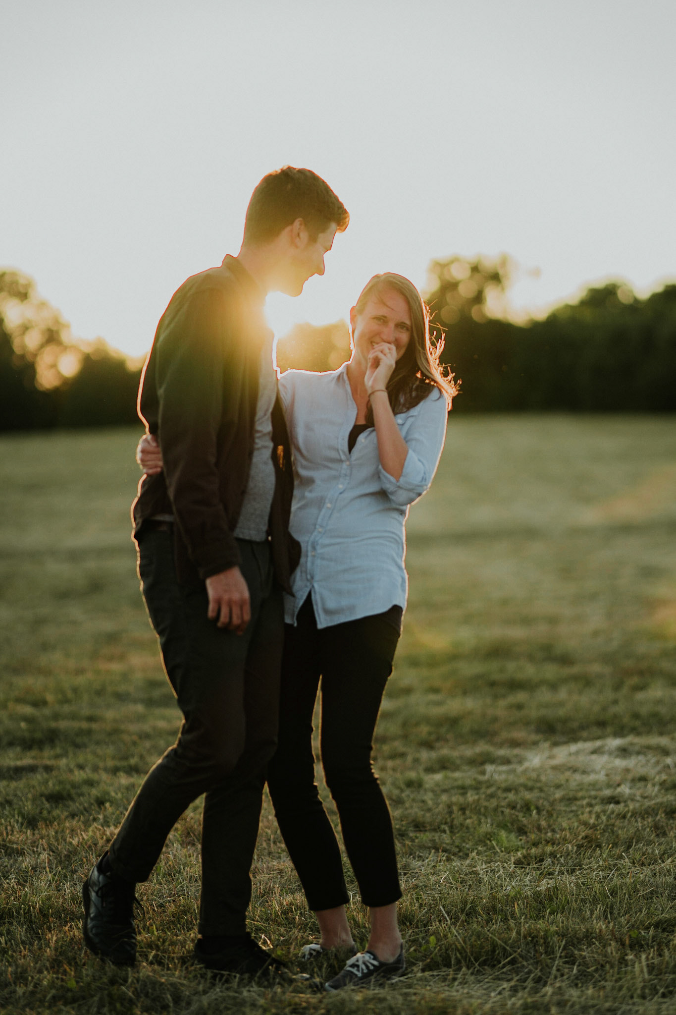 A couple laugh together in golden light. Taken during and engagement photoshoot in Wimbledon
