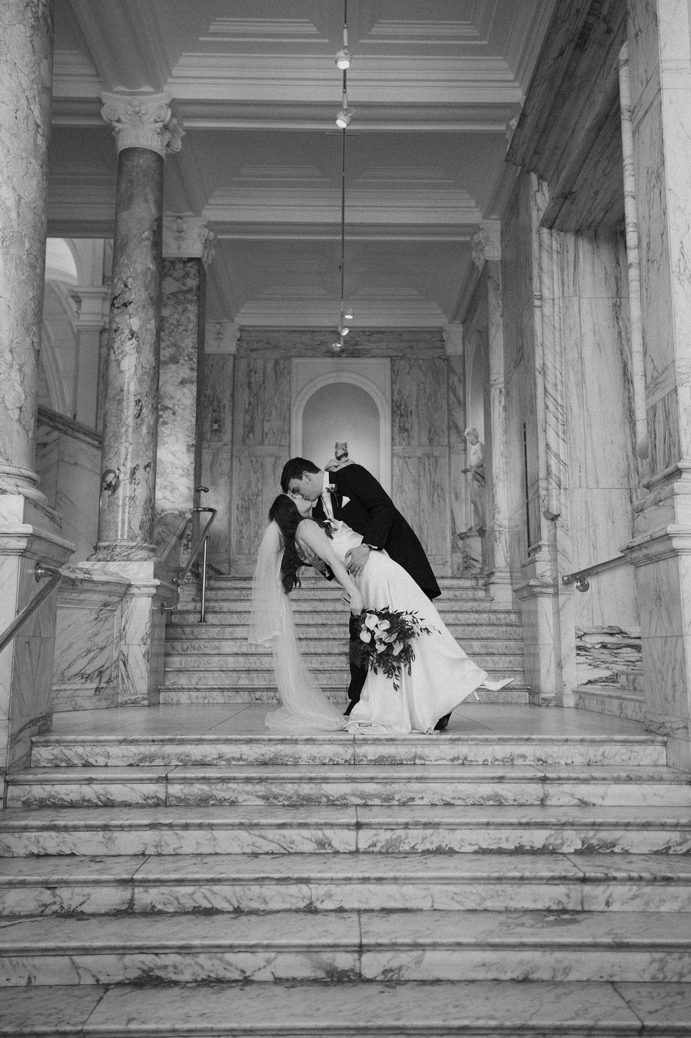 The groom kissing the bride on the grand staircase of the Victoria and Albert museum. 