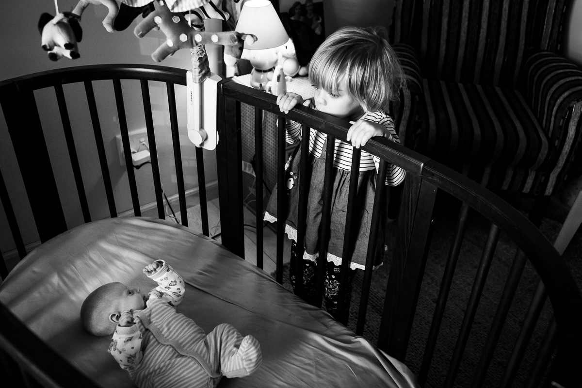 Big sister looking over cot at baby brother