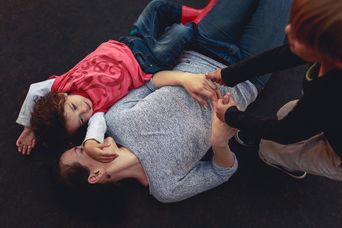 Mother and son lying down while other boy tries to pull her up