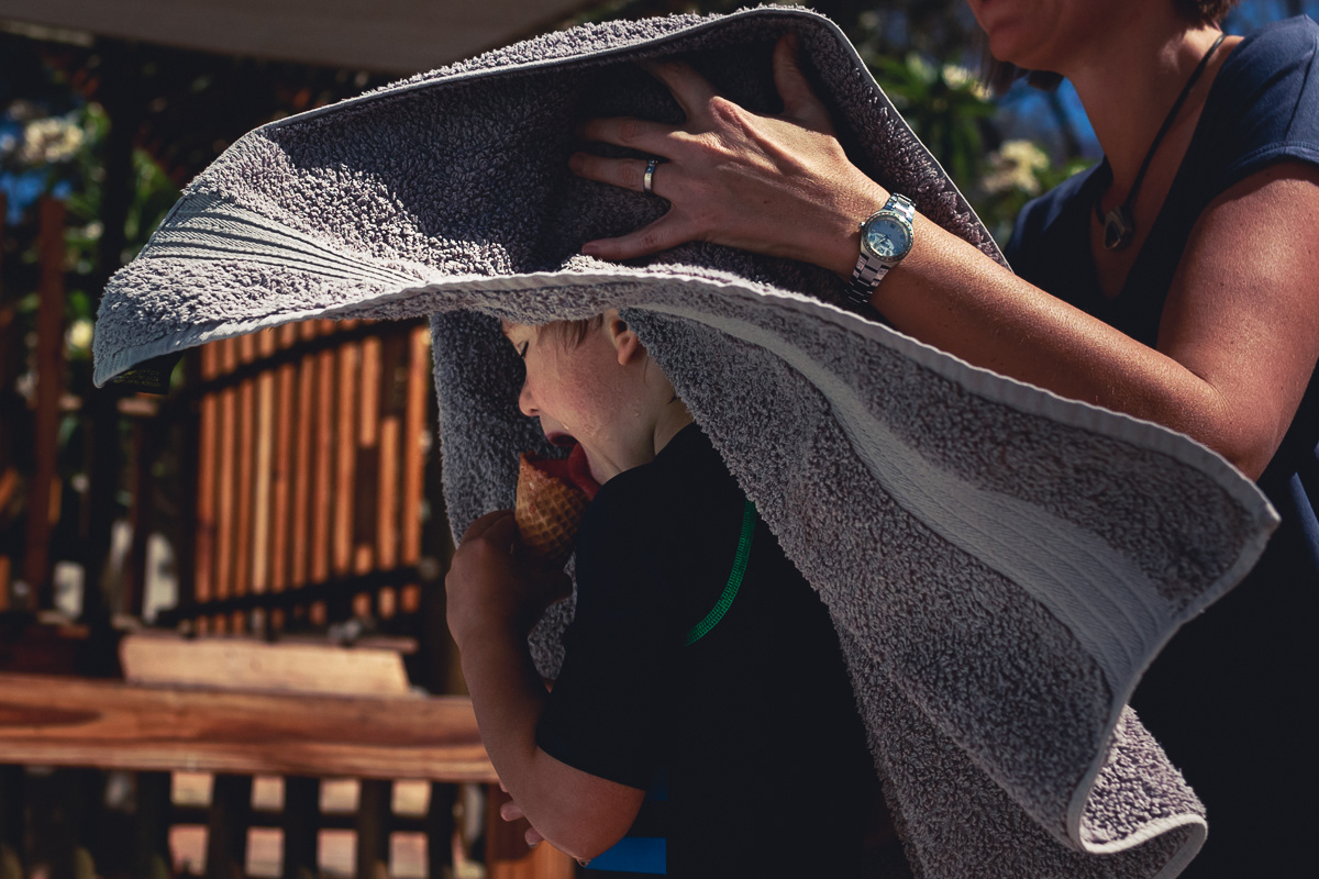 Boy eating ice cream while mom's drying him with a towel