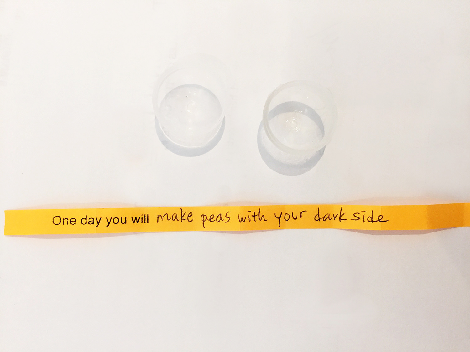 An empty clear plastic ball and a long piece of yellow paper with the text One day you will make peas with your dark side