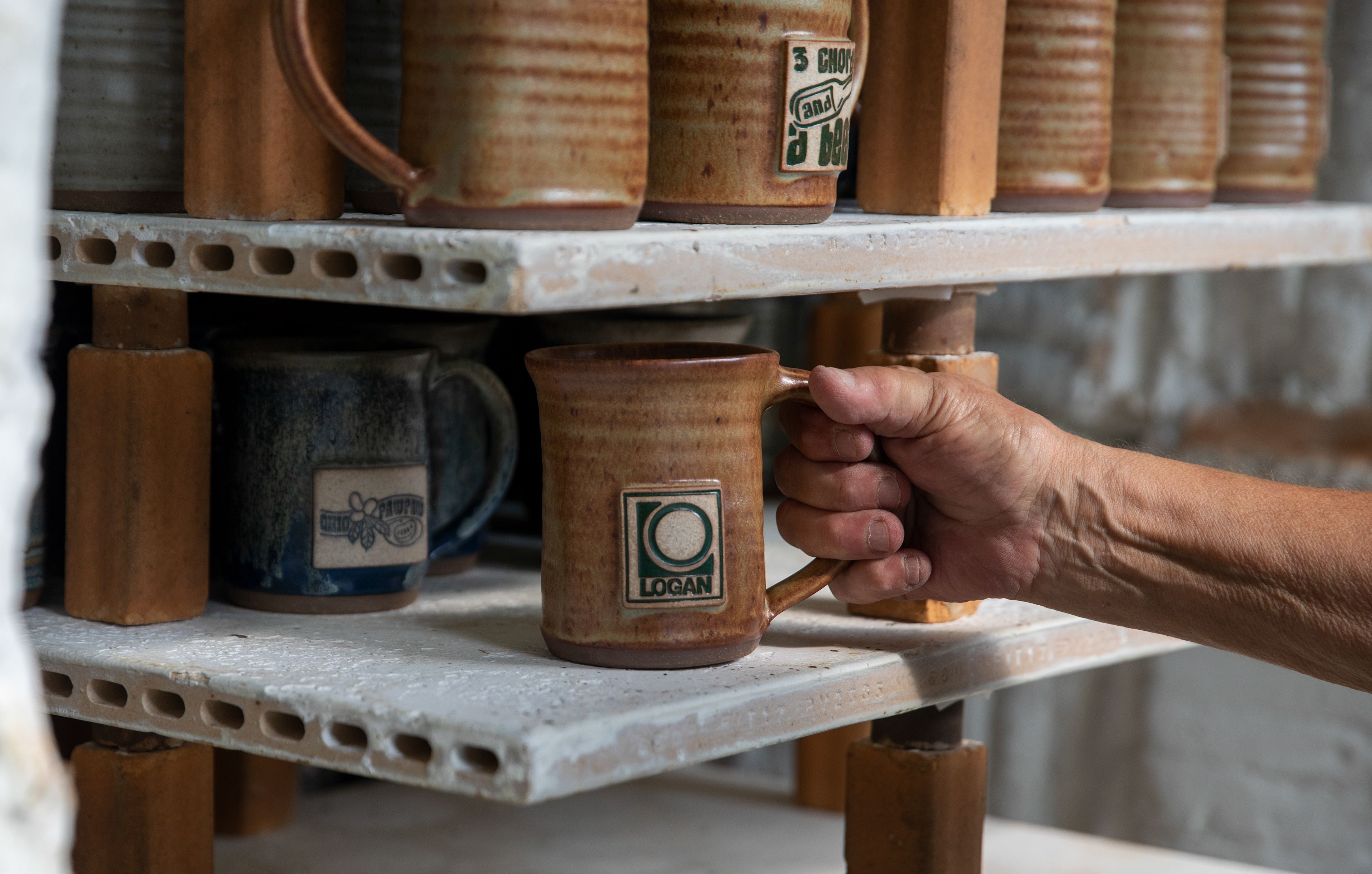 Susan Abramovitz’s hand unloading a mug from her outside kiln at her property and studio, Rock Riffle Run Pottery on September 14, 2022.