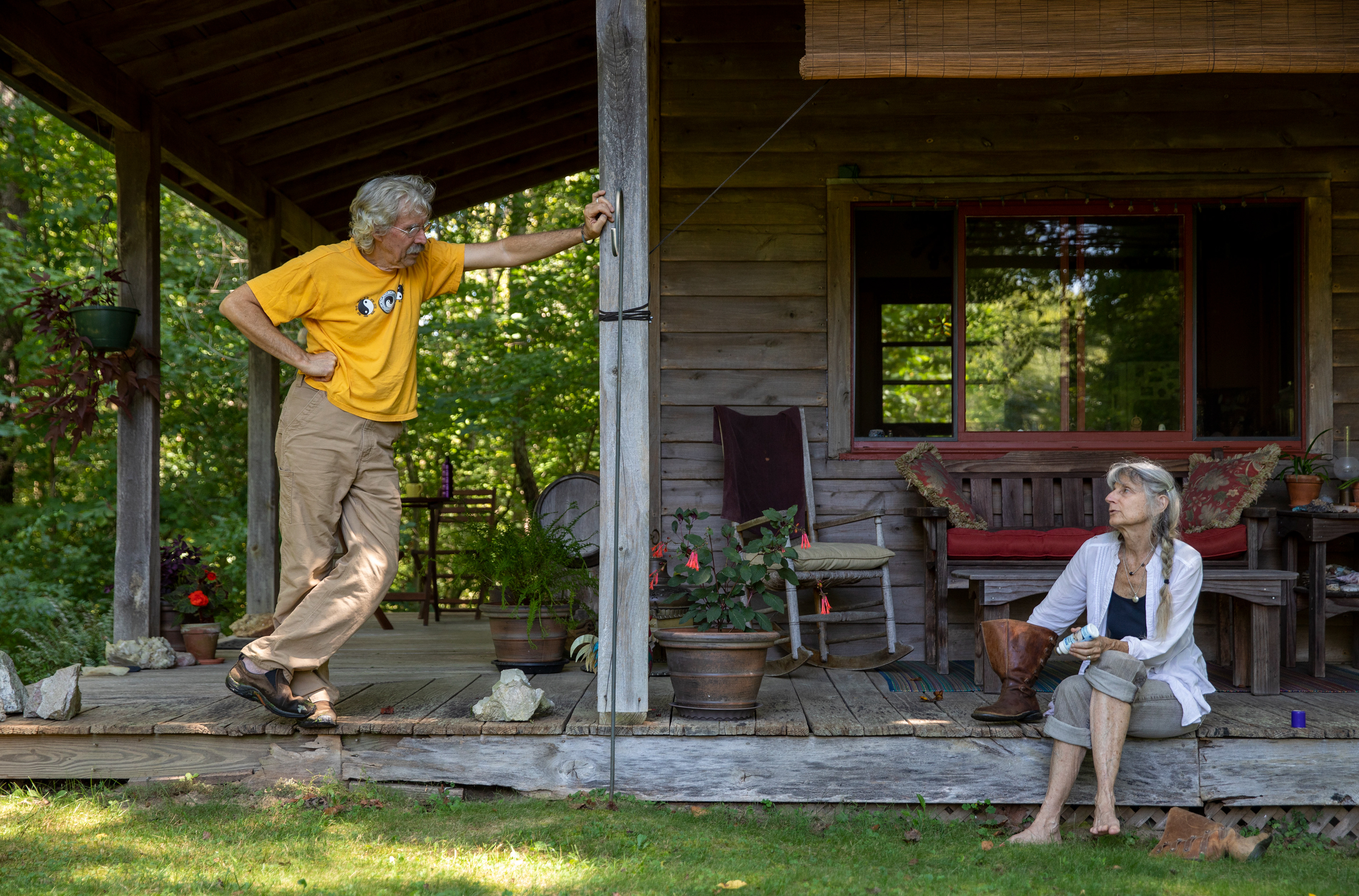 Phil Berry, 67, and Jo Merkle, 69, on their cabin porch chatting about the broken lawn mower as Jo applies a cleaner to her leather boots at their home in Rome Township, Ohio on August 28, 2022.