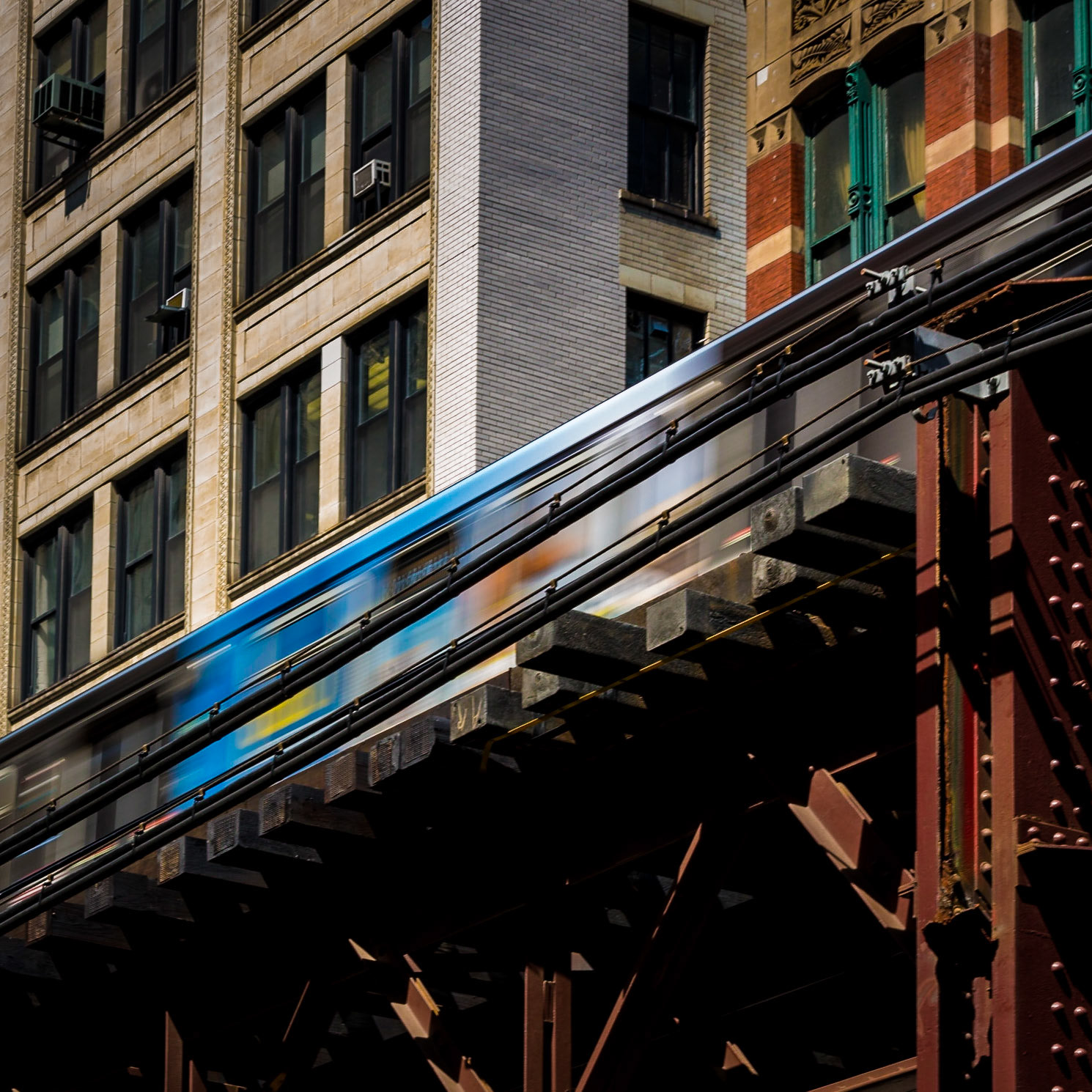 Swoosh. A CTA El train blurs past the buildings it traverses in the late afternoon sun of Chicago's Loop.