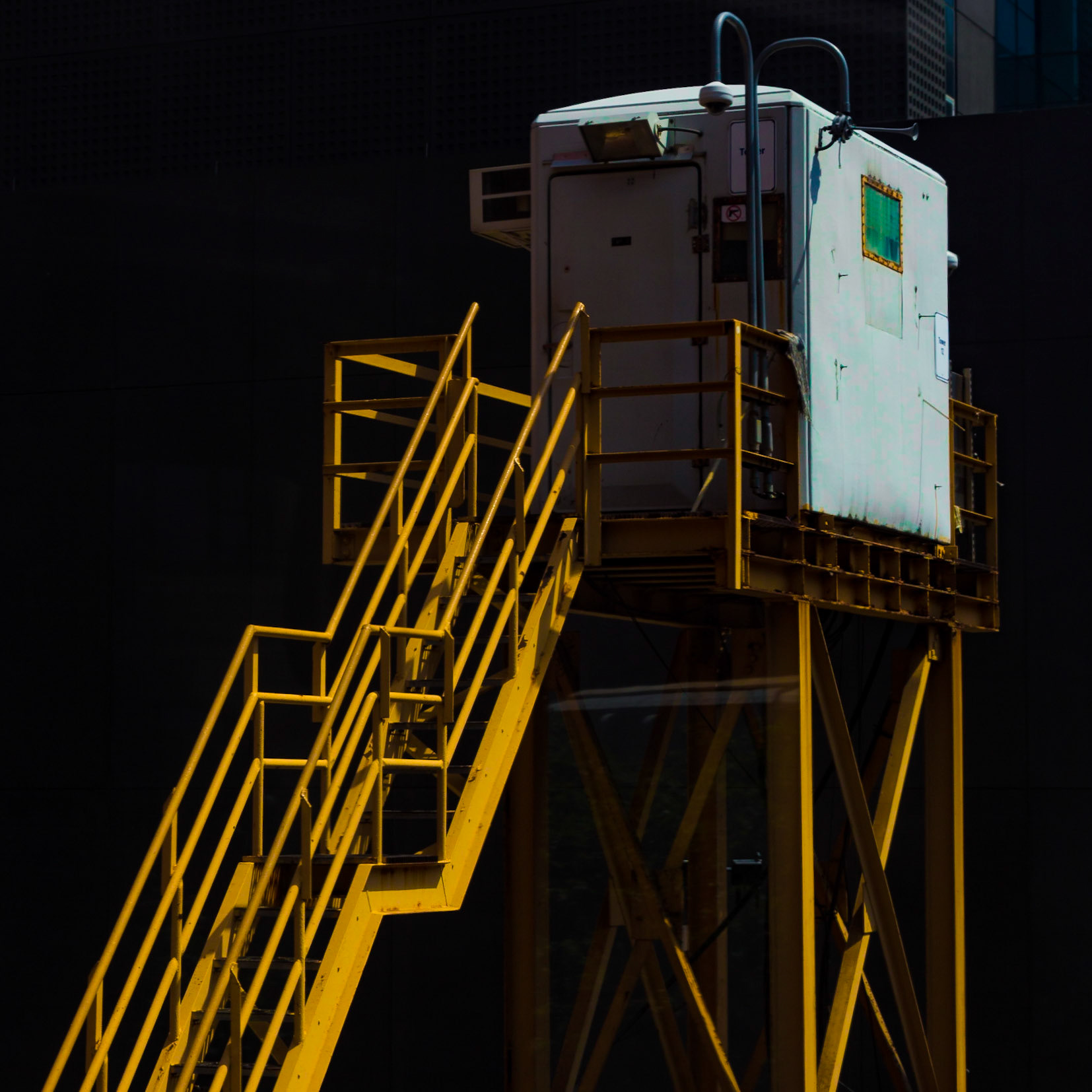 Room Without A View. Bold yellow steel stairs lead to a control box room with an opaque green window overlooking the Chicago El tracks.