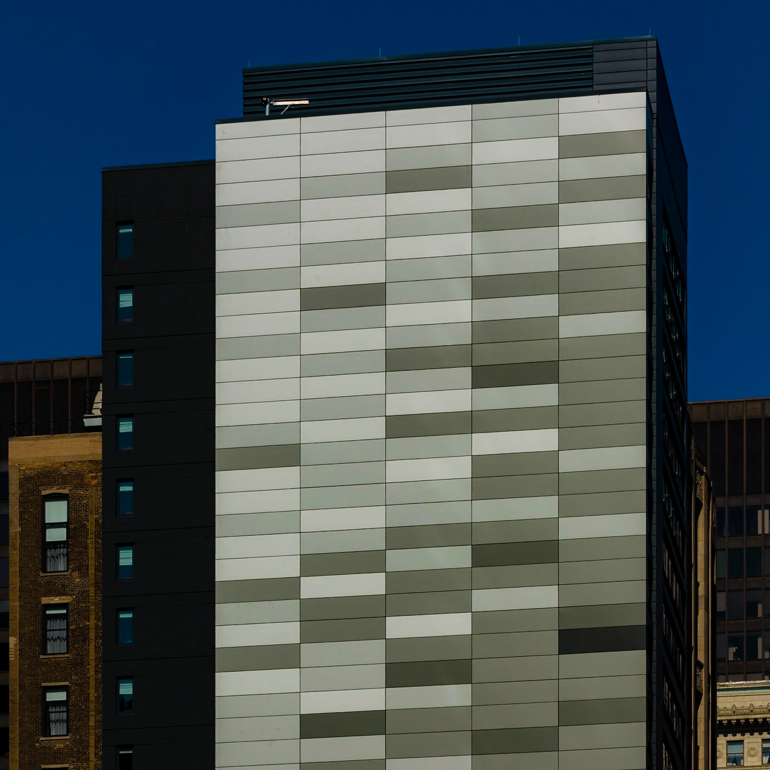 Movement in monolith. Using flat blacks to let the utility portions of the building recede, the mosaic of greyscale panels glint in the sun, as if window reflections along the moving tracks of an el train.  I love the motion of this facade treatment.