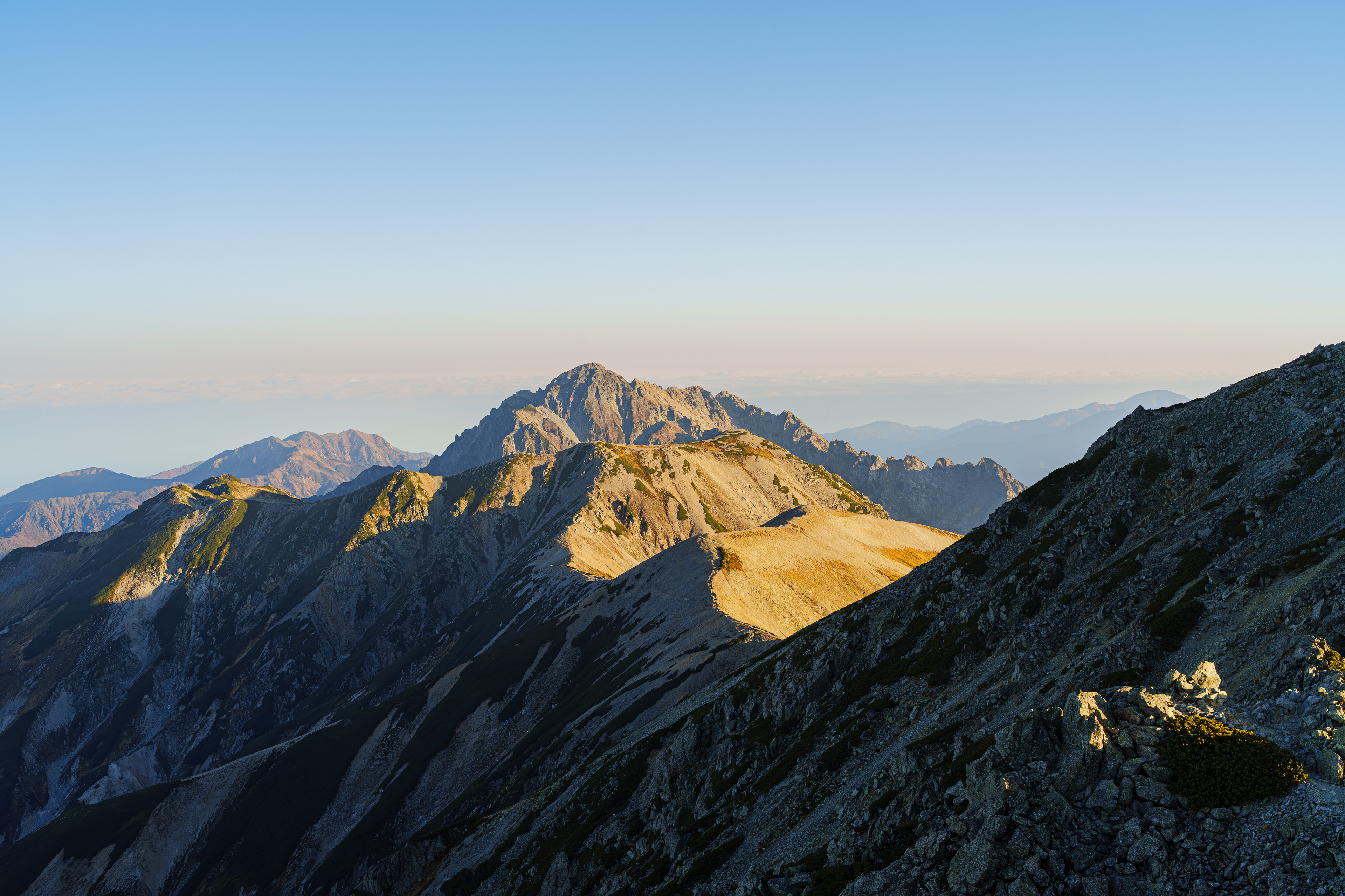 日の出を雄山山頂で見る予定だったが小休憩をしっかり取った事と、強風の影響とゆっくり歩いたことで日の出時刻には間に合わなかった。15分程過ぎて山頂に着くと東側は雲が多く時間通りに来れても結局見れなかった。それから30分後ぐらいに雲の隙間から太陽を見ることができた。南側は晴天。雲の隙間からの陽の光がこれから歩く稜線を照らしていた。  2025/10/23　雄山山頂
