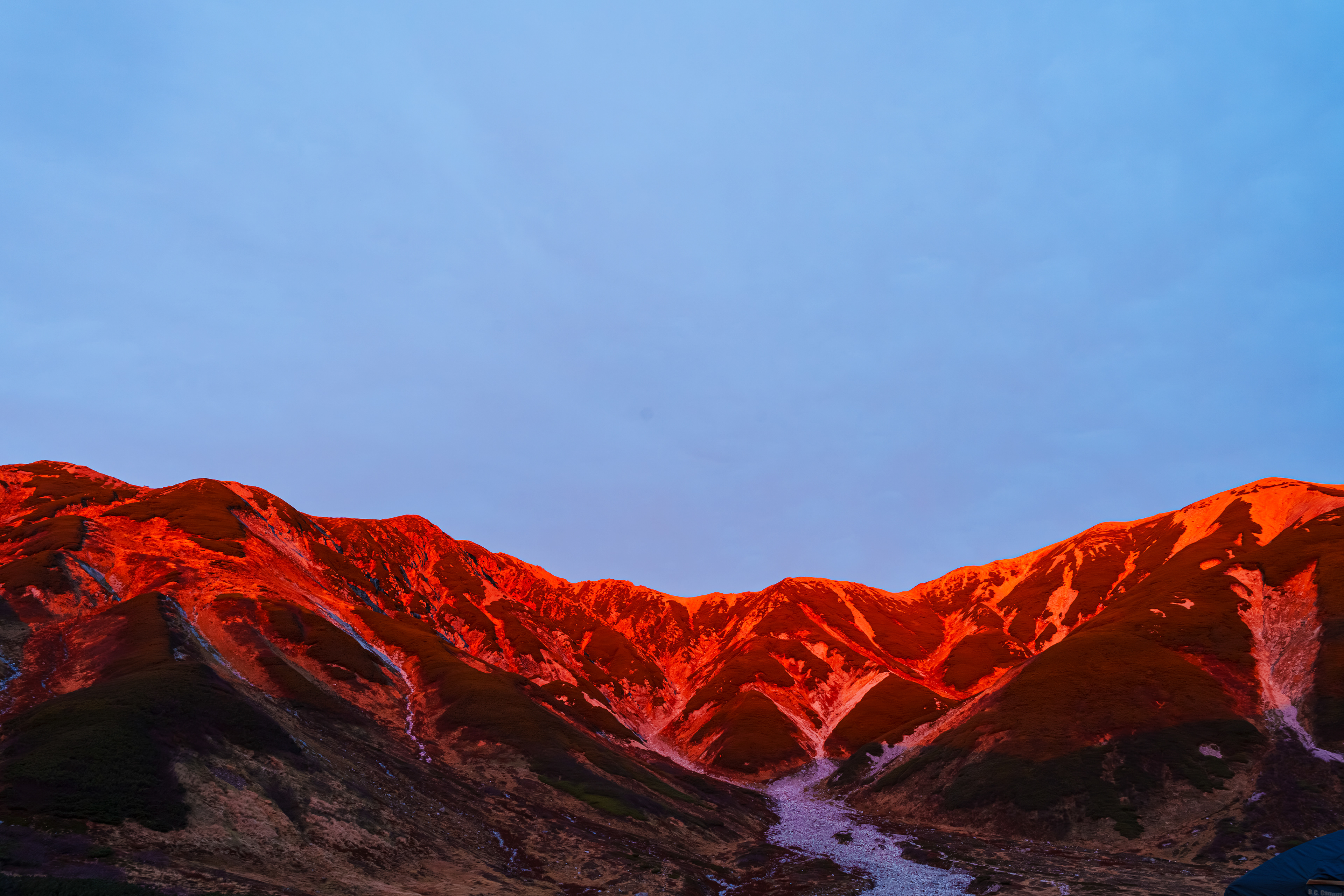 テン場について設営をしてから昼食。食事を済ませてからテントの中で休憩。動かず昼食を食べてゆっくりしていたので体の芯まで冷えた。嬉しいことに15分程登ると雷鳥荘に温泉があり入浴できるので、少し早いが15時から温泉に入った。剣山が見える贅沢な浴槽で1時間ゆっくりと温まった。温泉から上がり休憩をしてからテン場に戻る。日没が17時15分、テン場は陰になり暗くなり始めていた。夕食の準備をしていると外がいきなり明るくなった。急いで出てみると雲が抜け空は青く山肌が夕日で赤く染まっていた。燃えているようだった。  2025/10/22　雷鳥沢テント場