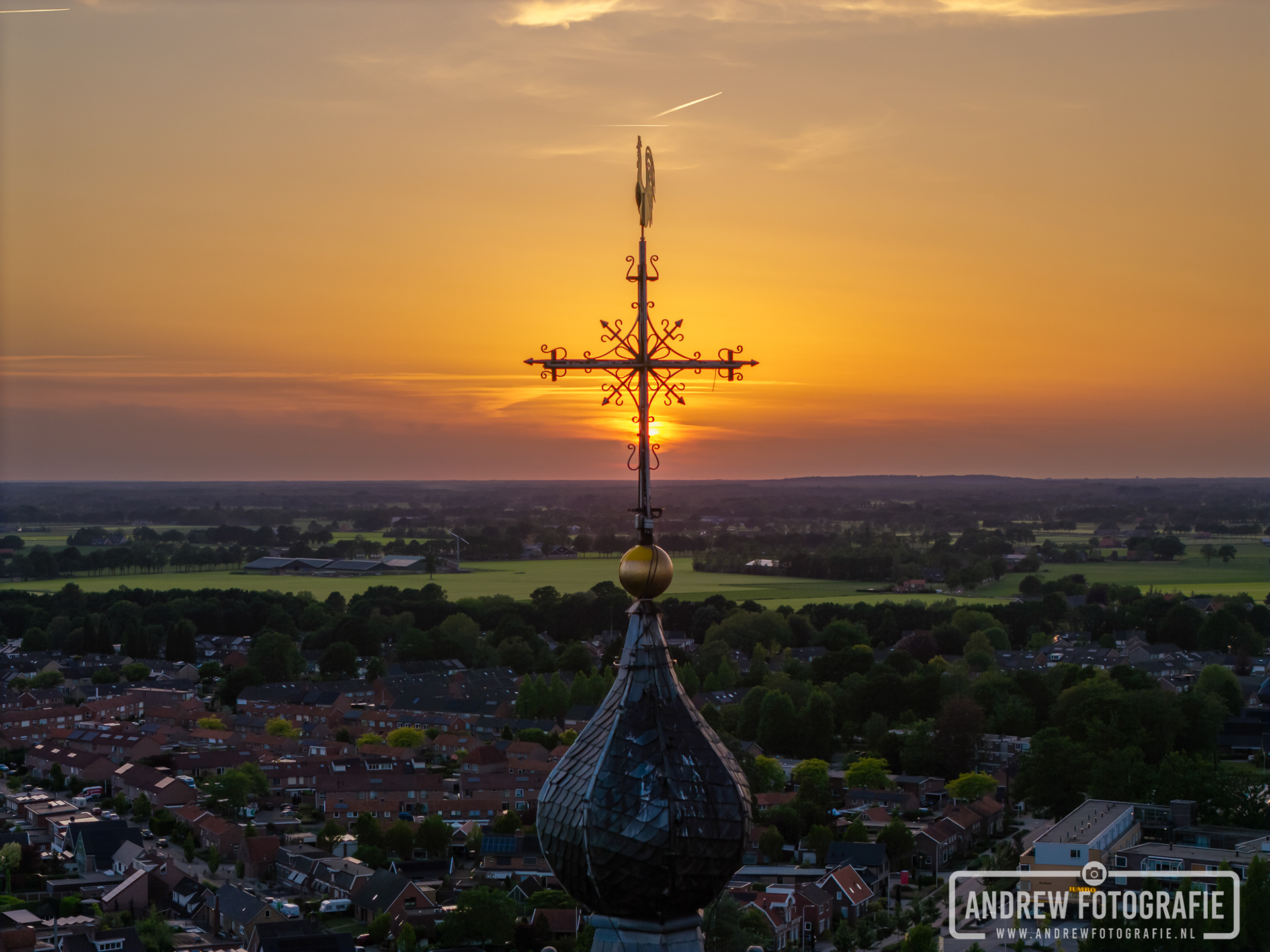 Close-up van het ijzeren kruis op de kerktoren van de Calixtusbasiliek tegen een goudgele Achterhoekse lucht.
