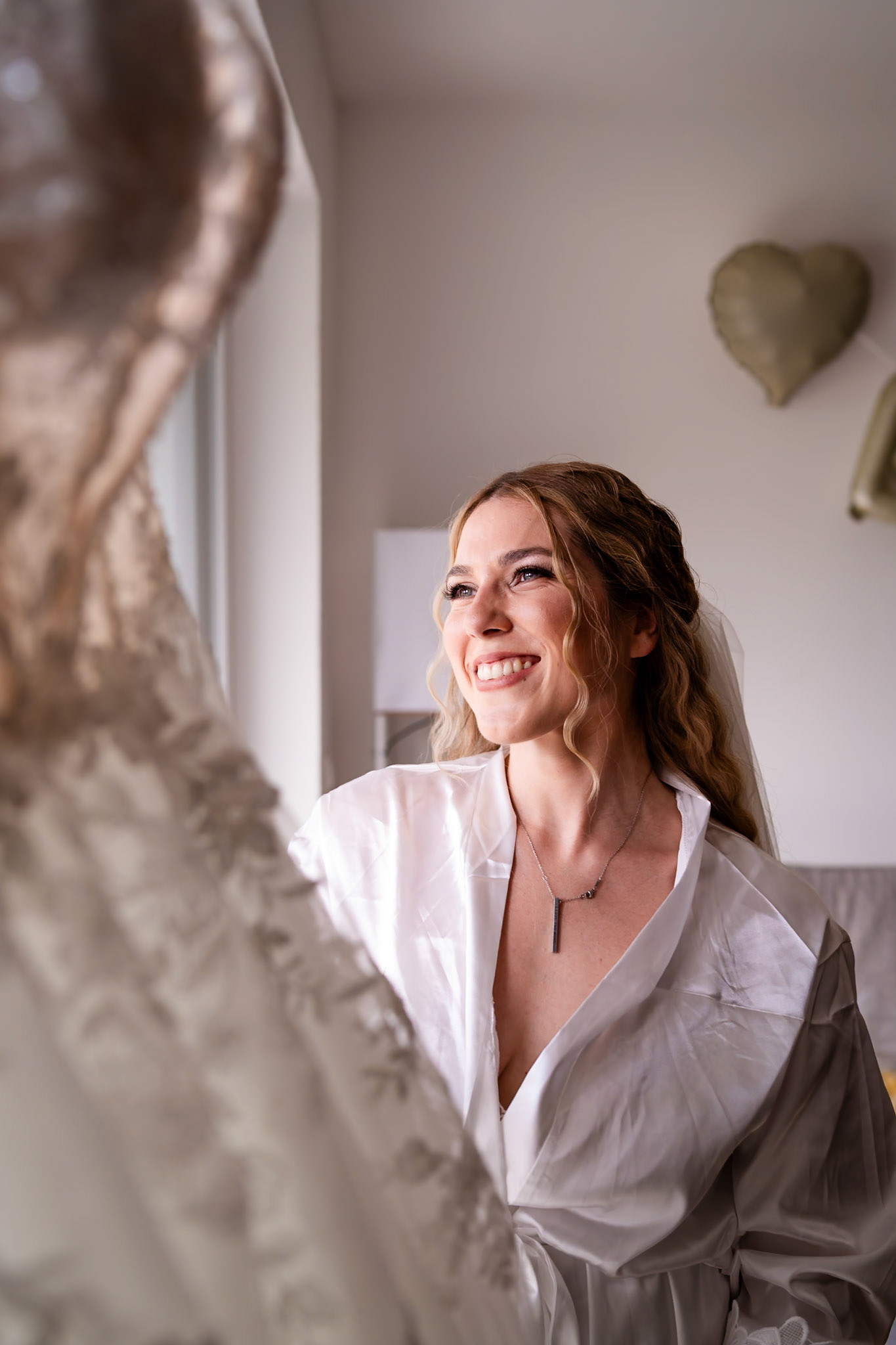 Vorfreude beim Getting Ready: Lächelnde Braut betrachtet ihr Hochzeitskleid – MFuchsloch Hochzeitsfotografie & Videografie
