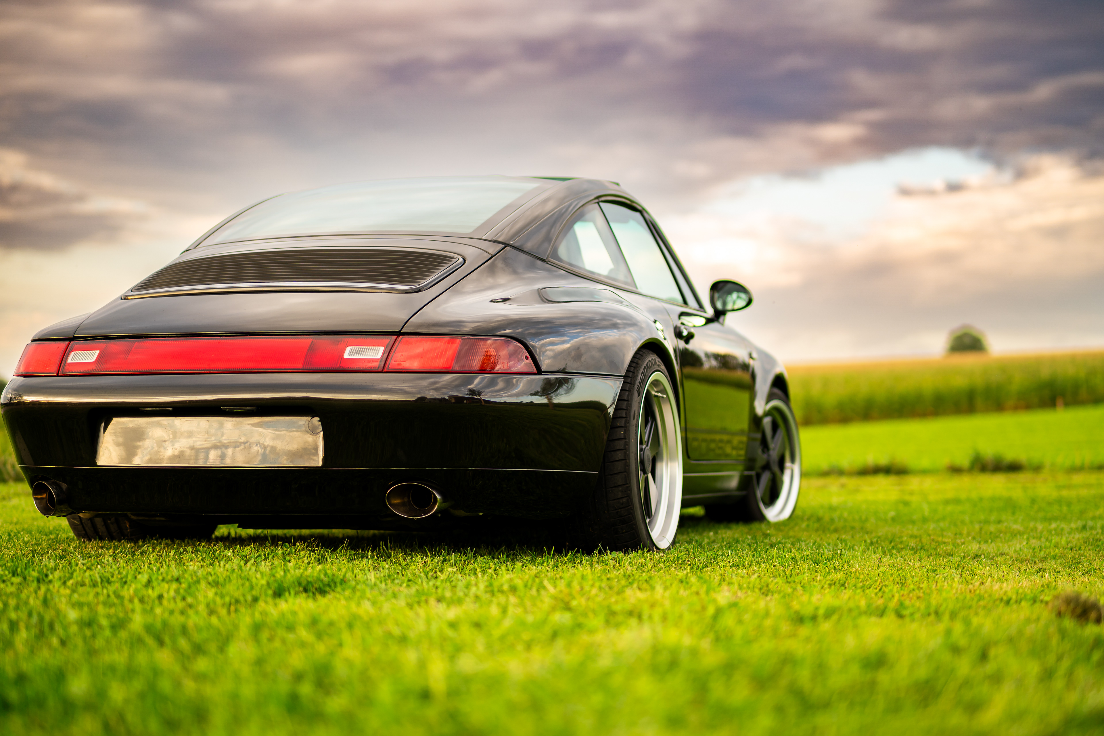 Klassischer schwarzer 1997 Porsche 993 Targa auf einer Wiese in Oggelshausen am Federsee während des Sonnenuntergangs. Hochwertige Automotive Art und professionelle Fahrzeugfotografie von MFuchsloch Fotografie & Videografie aus Oberschwaben.