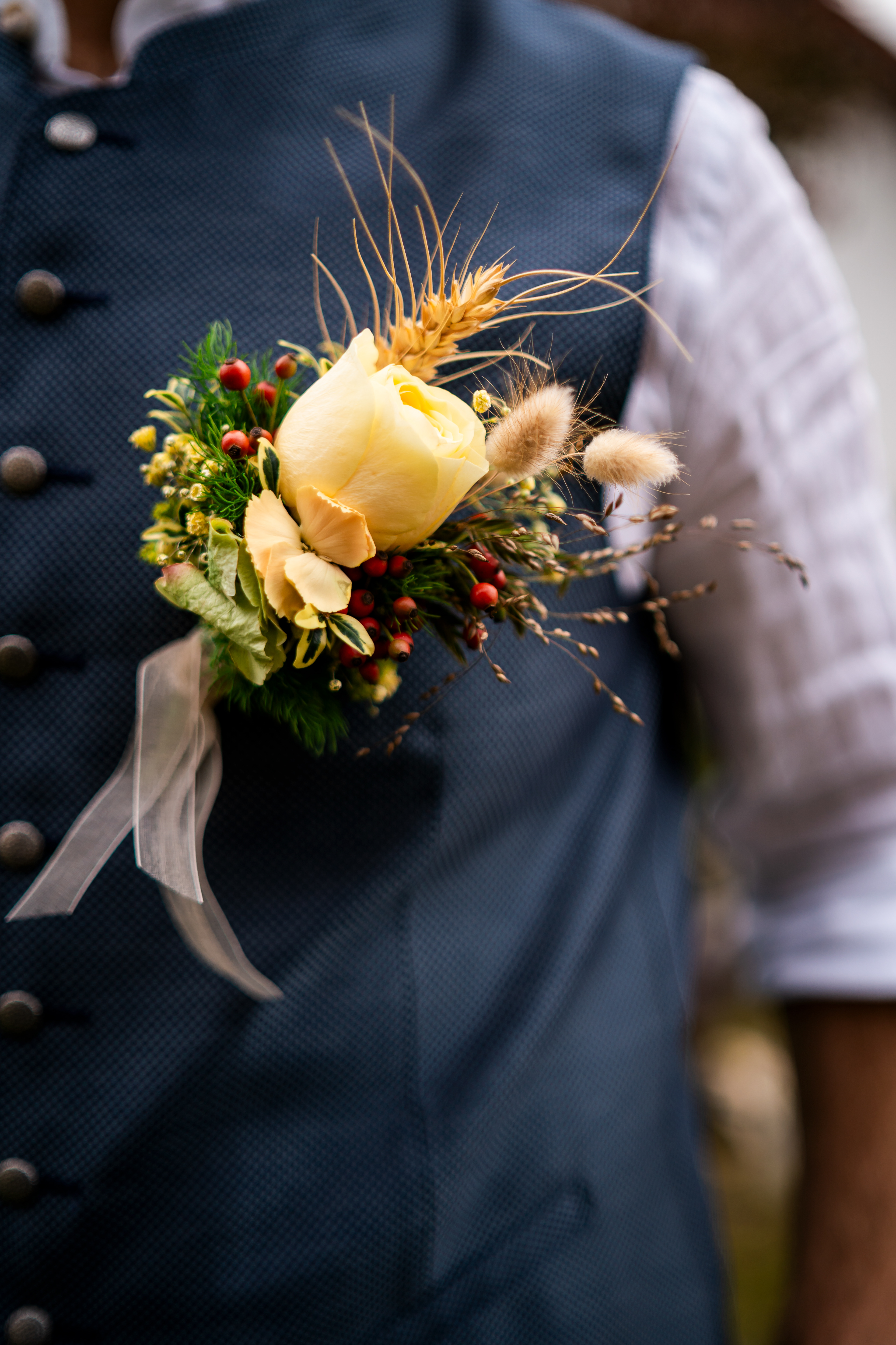 Detailaufnahme des Bräutigam-Ansteckers mit gelber Rose und Weizen – passend zur Trachtenhochzeit. Fotografiert von MFUCHSLOCH Fotografie & Videografie.