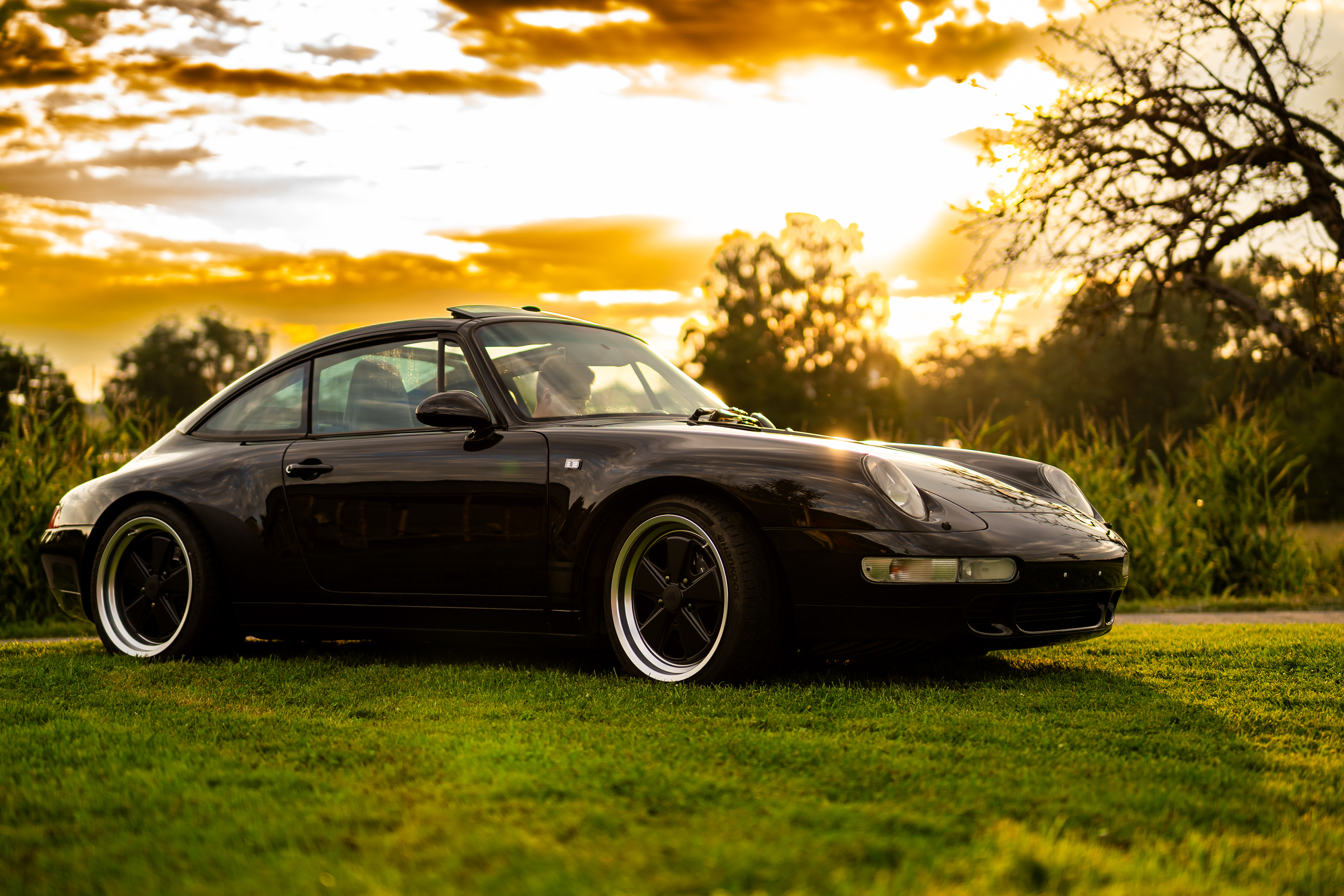 Klassischer schwarzer 1997 Porsche 993 Targa auf einer Wiese in Oggelshausen am Federsee während des Sonnenuntergangs. Hochwertige Automotive Art und professionelle Fahrzeugfotografie von MFuchsloch Fotografie & Videografie aus Oberschwaben.