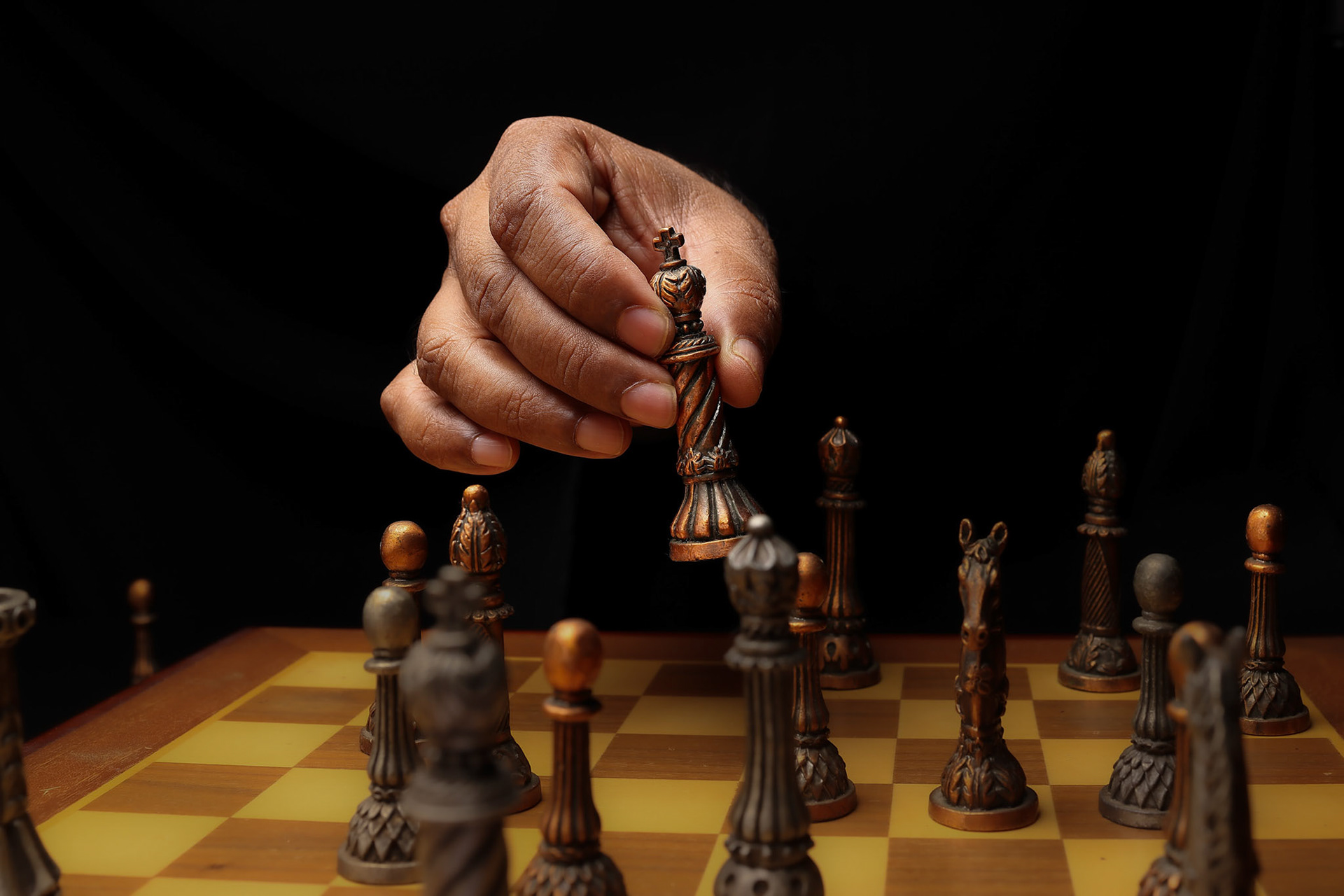 Asian male dark skinned single hand fist finger on black background holding chess game piece king soldier pawn playing making move checkmate