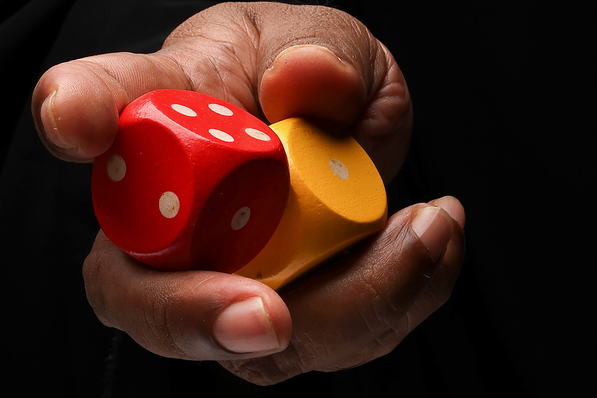 Asian male dark skinned single hand fist finger on black background holding wooden red yellow playing dice
