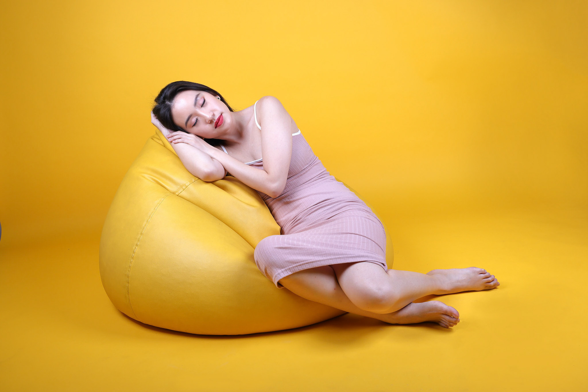 Beautiful young south east Asian woman sit on a yellow orange beanbag seat color background relax rest think emotion imagine expression pose sleep