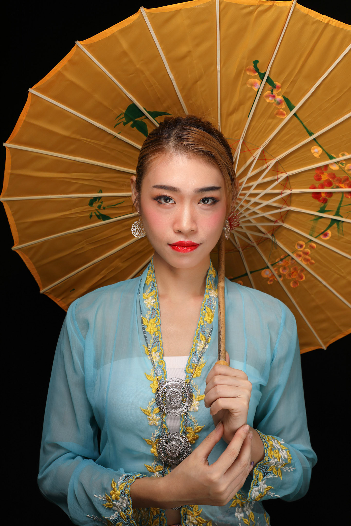 Asian woman in tractional kebaya behind umbrella on black background