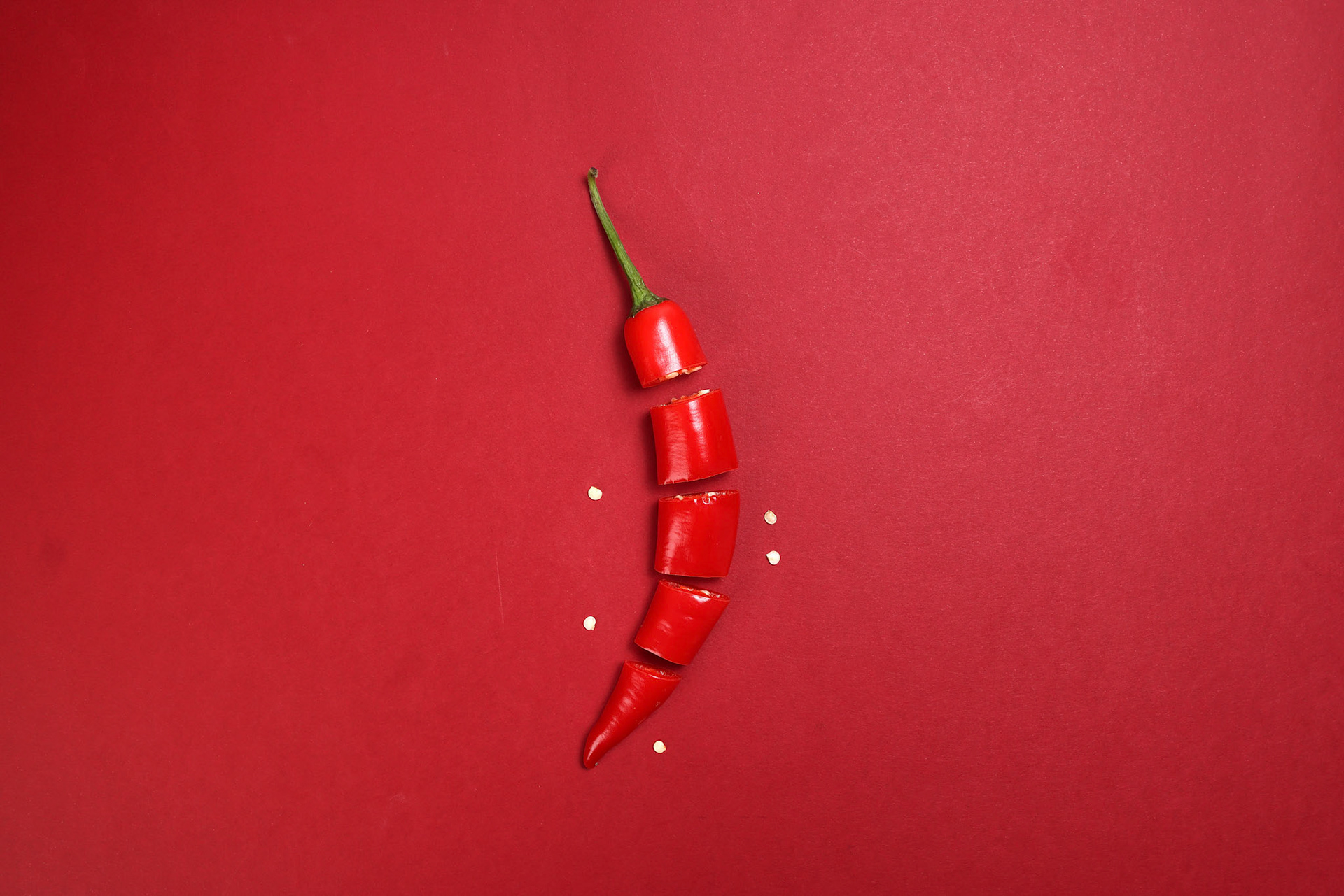 red chilli pepper on red paper background cut pieces seeds