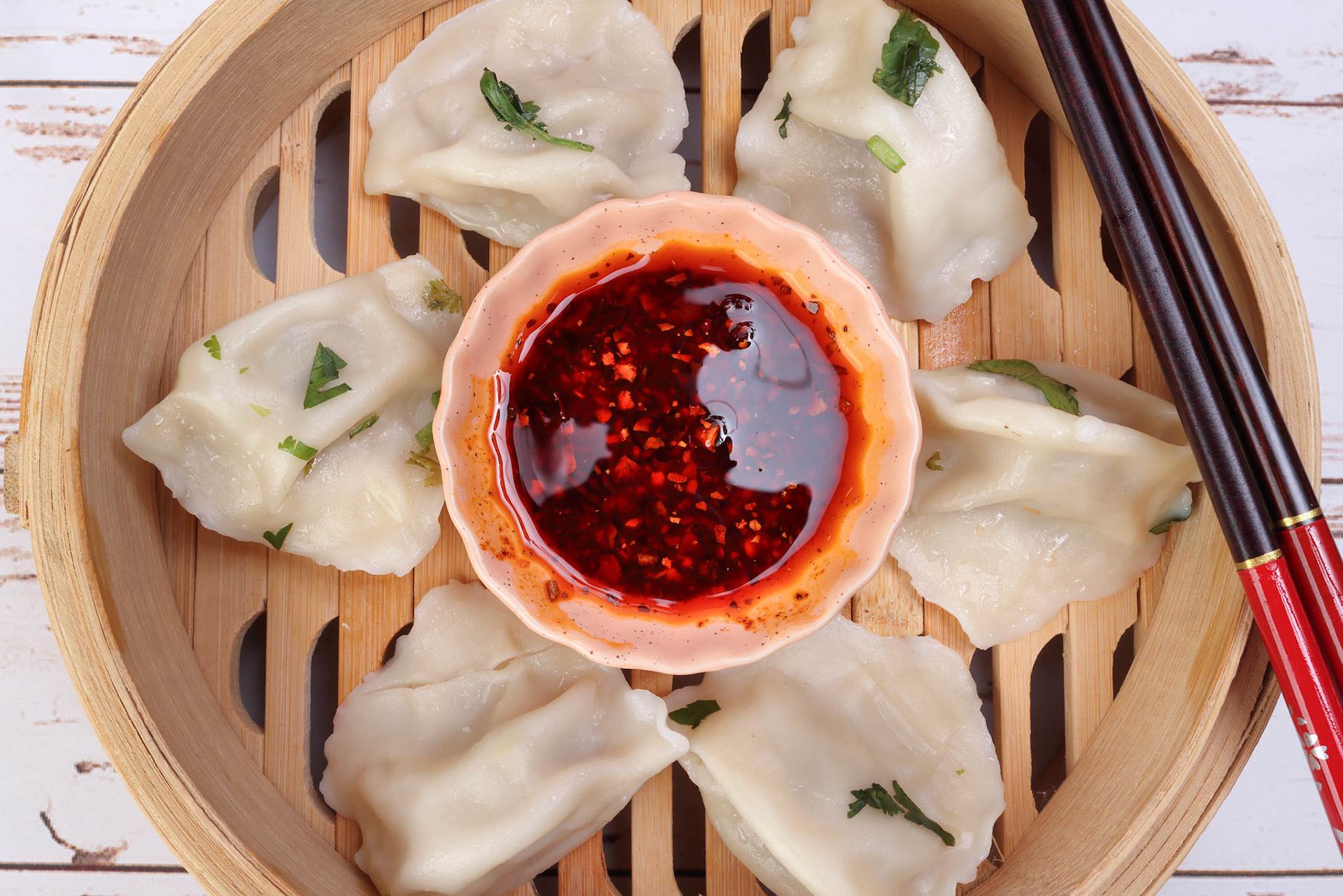 Home style dim sum dumpling in bamboo steamer chopsticks chili flake oil sauce on rustic wooden background