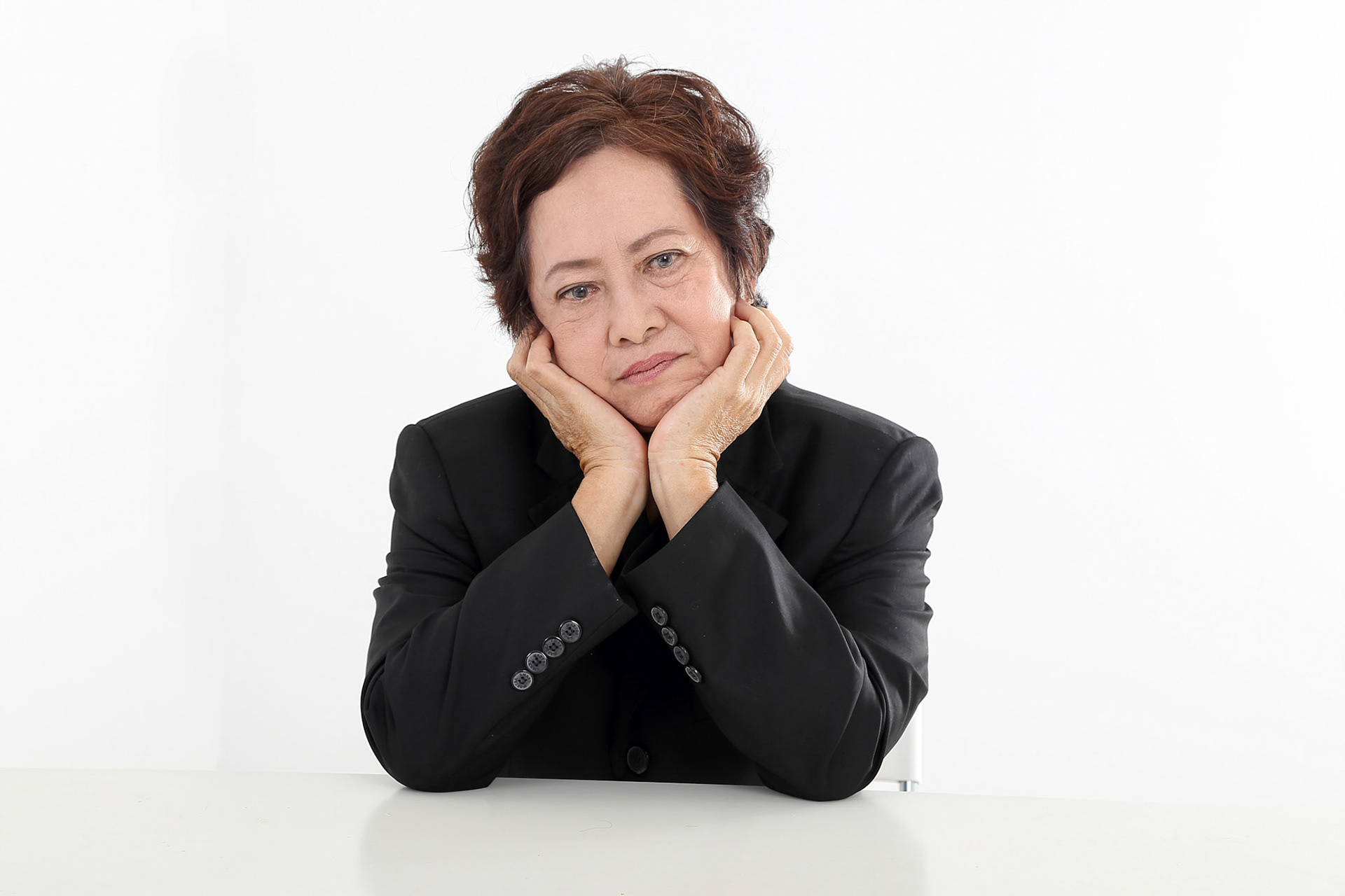 Elderly asian Chinese female on white background wearing black suit thinking hand on cheek look down