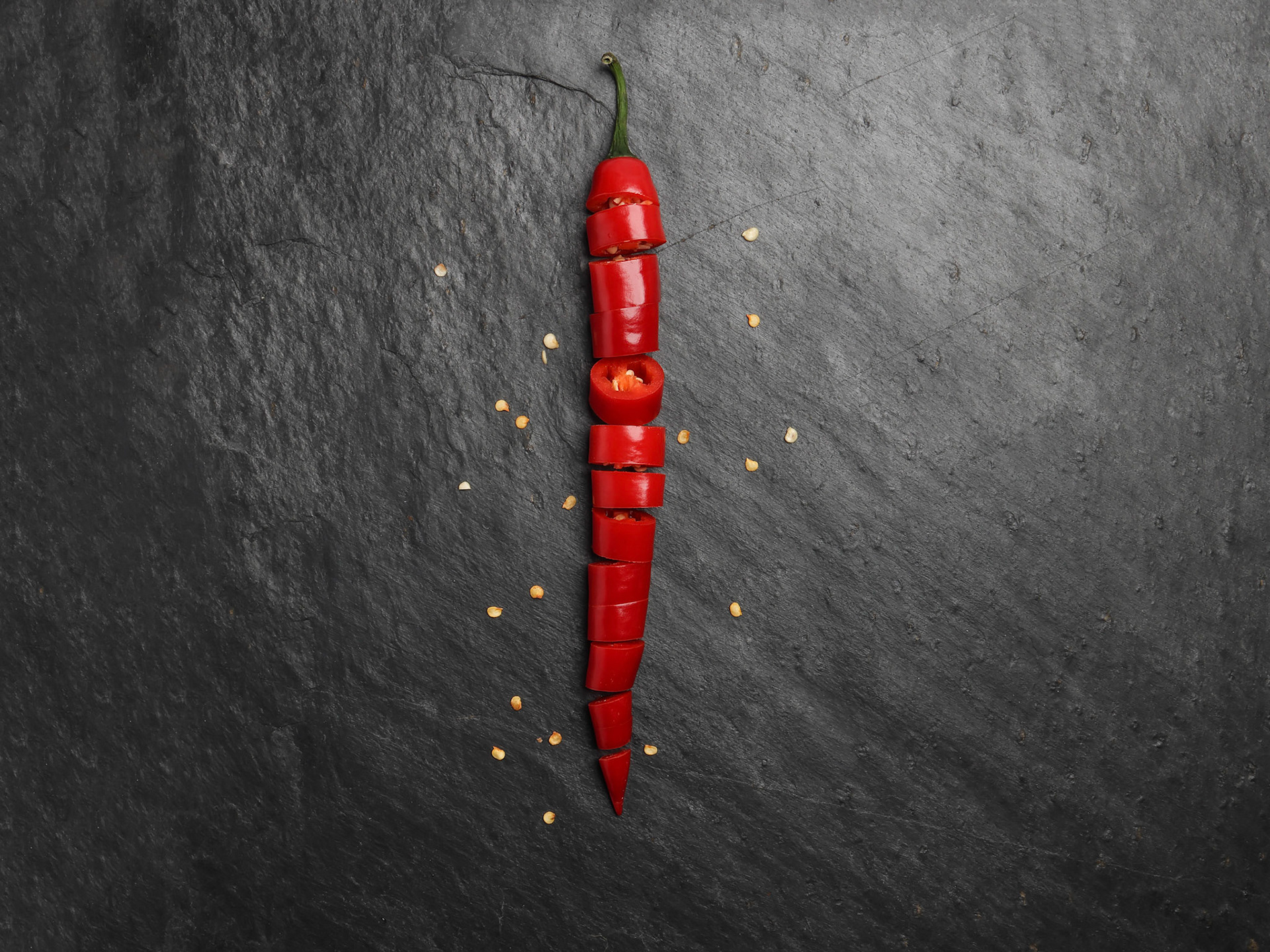 Red hot chilli pepper on dark black rough slate stone surface background