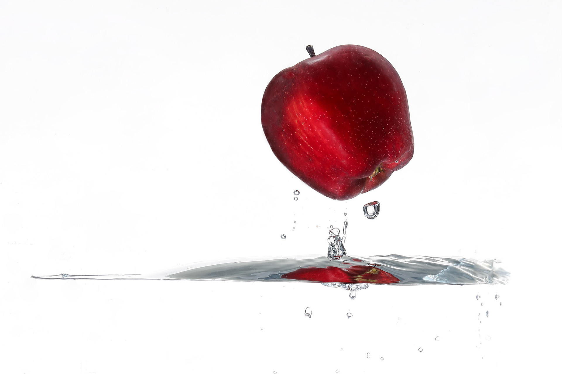 Red Apple splash wave ripple in water upside down white background