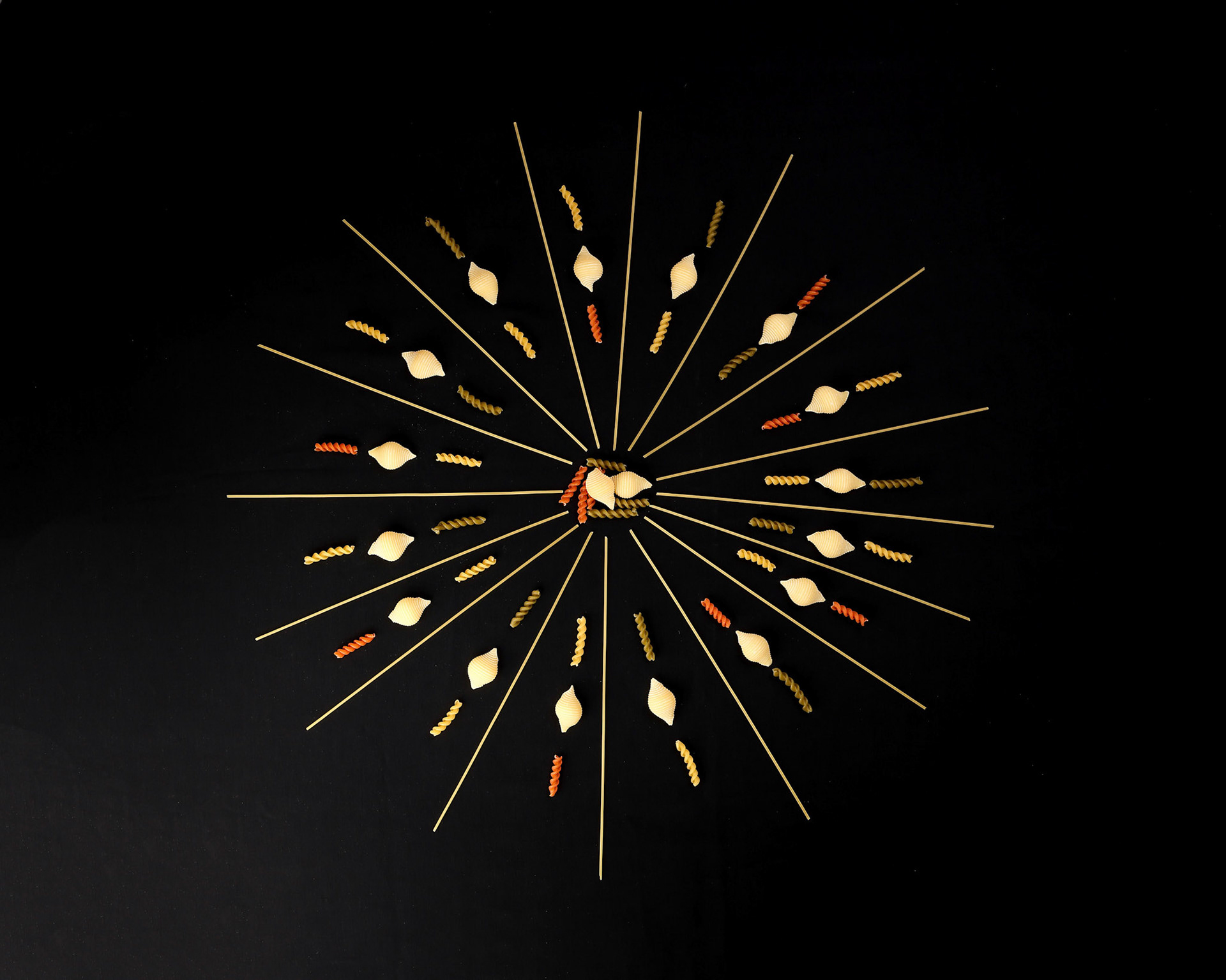 dry raw spaghetti conchiglie seashells fusilli cork screw color pasta laid on black background sunray glow pattern concept
