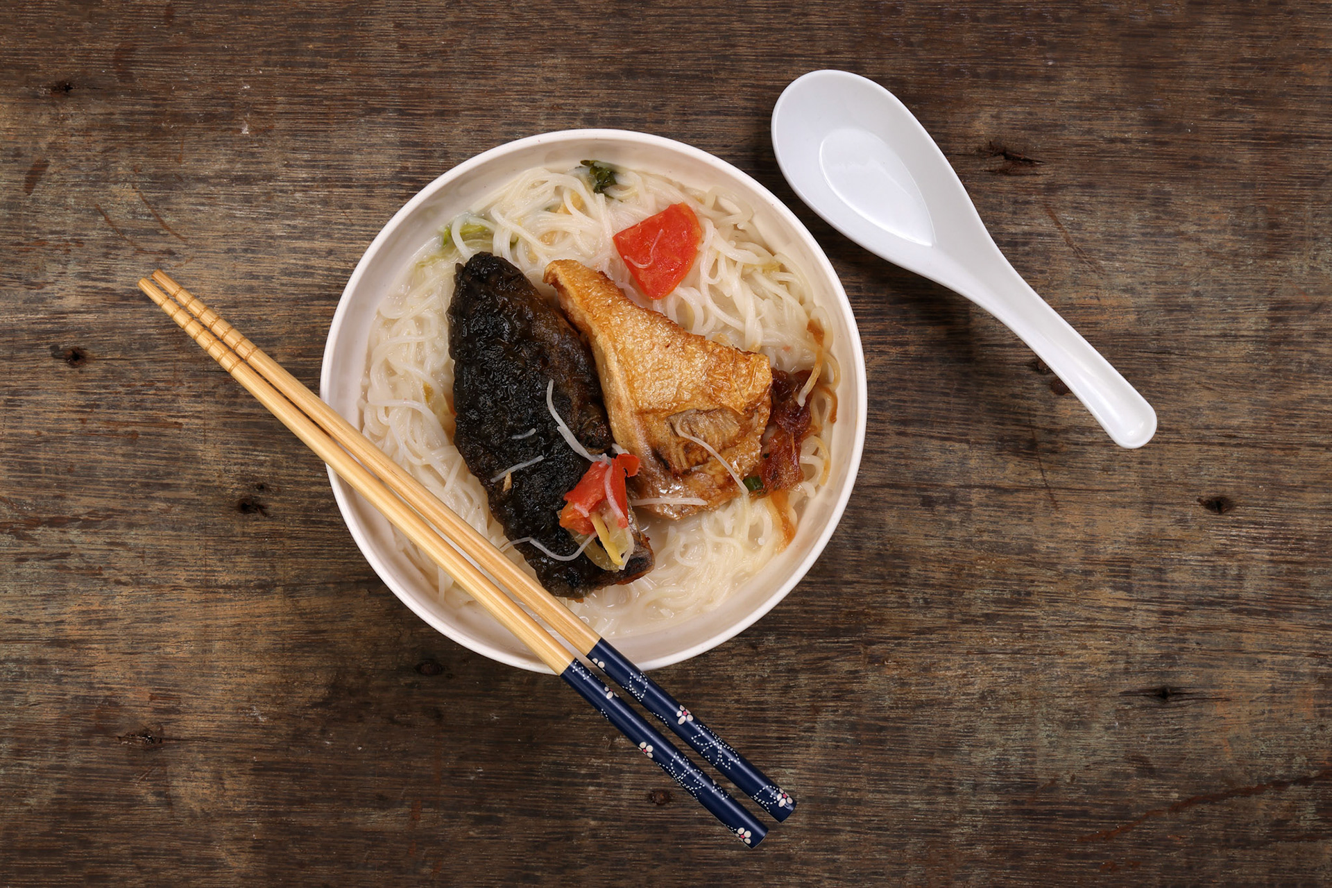 Fish head noodles vermicelli milk soup in white bowl chopstick spoon on rustic wooden background