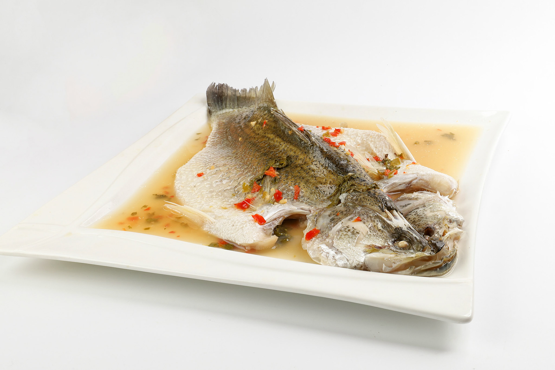 Thai style steam sea bass barramundi with lemon garlic chilli clear sauce on white serving dish