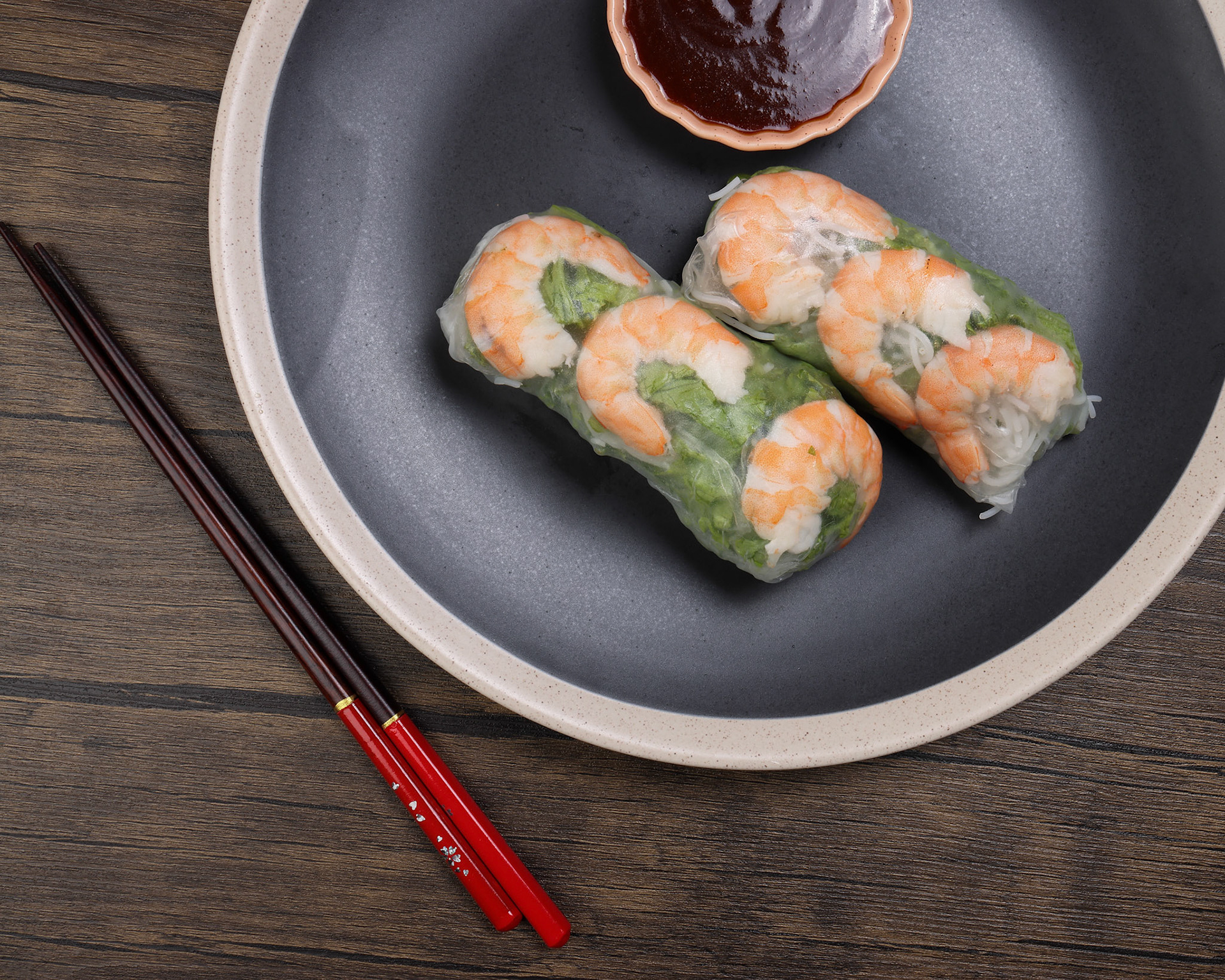 Vietnamese prawn shrimp see through rice paper spring roll green vegetable sauce on dark plate chopsticks wooden table