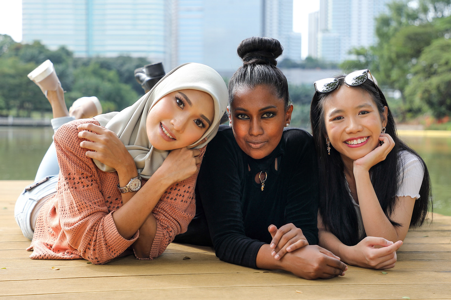 Three woman Malay Chinese Indian Asian Malaysian outdoor green park lake nature lying on front wooden deck hand on cheek talk smile chat emotion expression