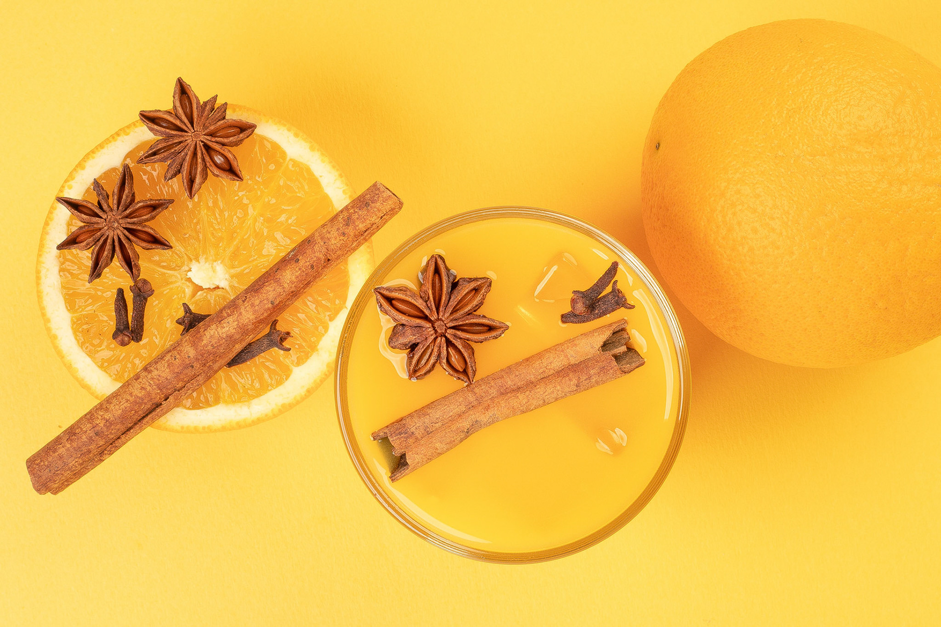 Fresh orange cinnamon star anise clove spice juice in glass on white yellow background