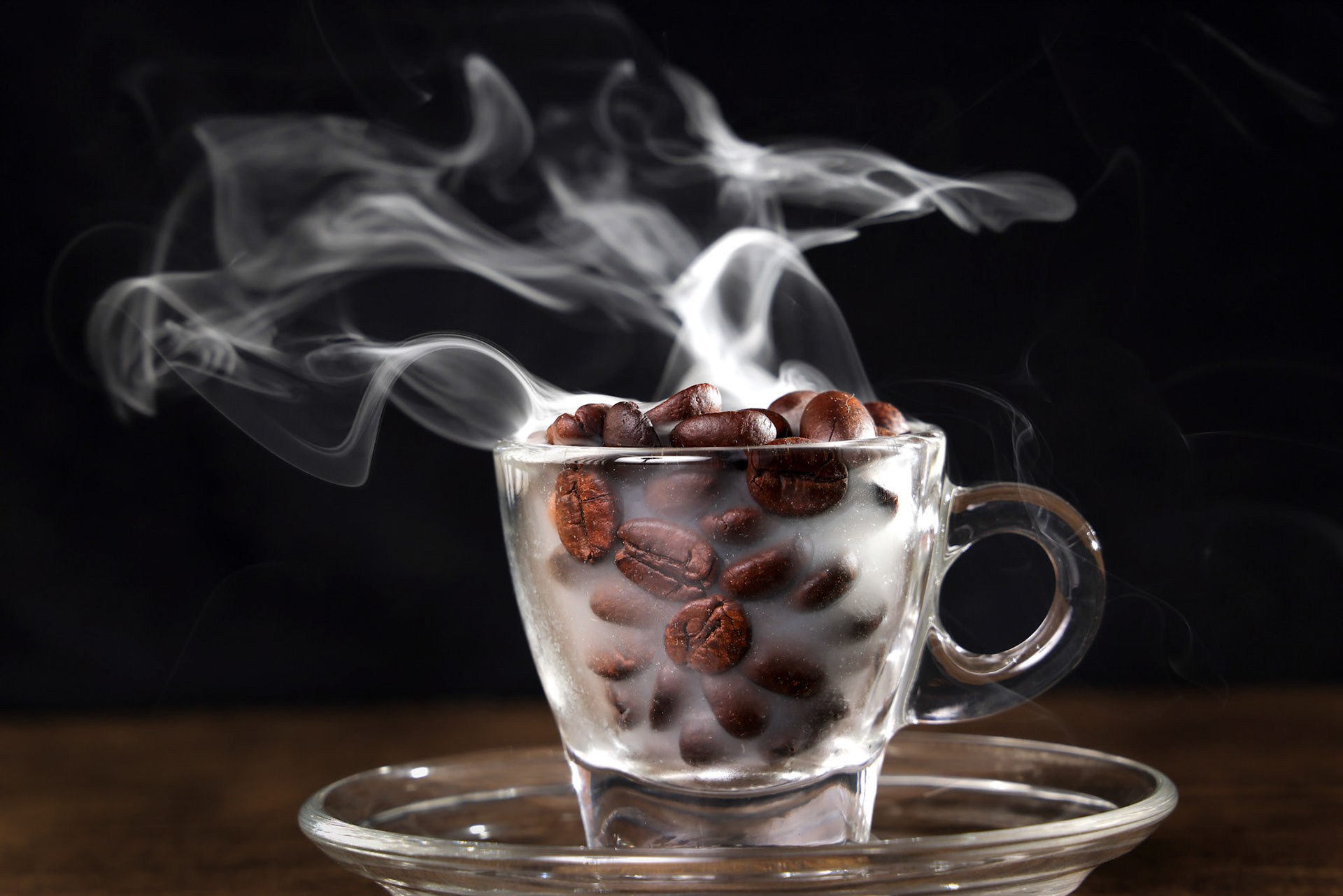 Smoke vape fog flowing out of transparent glass coffee cup filled with coffee beans on dark black background