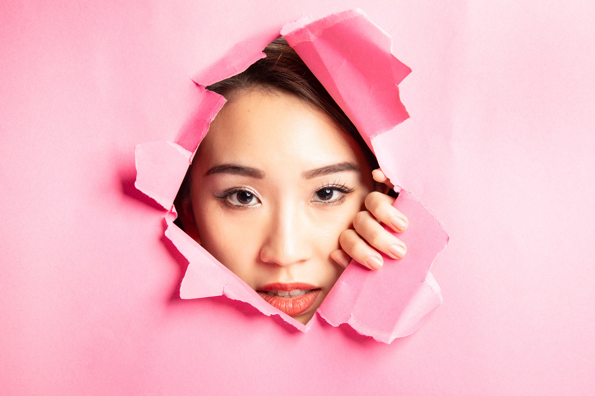 Young beautiful Asian woman expression through torn paper hole