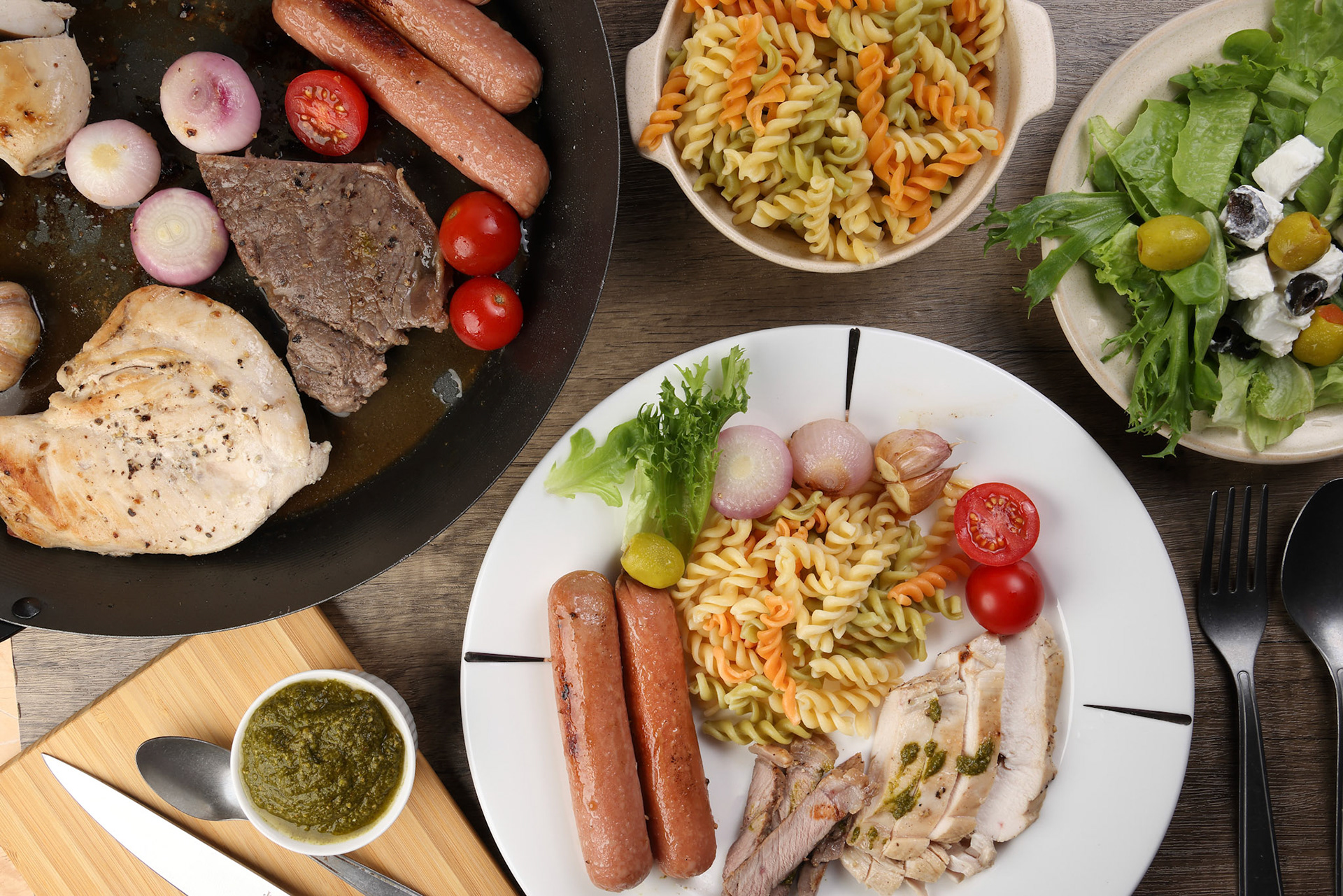 Mix meet chicken beef steak sausage tomato onion garlic fry grill metal pan colorful pasta green salad cheese olive mint basil pesto sauce board knife fork spoon sliced served plate wooden table