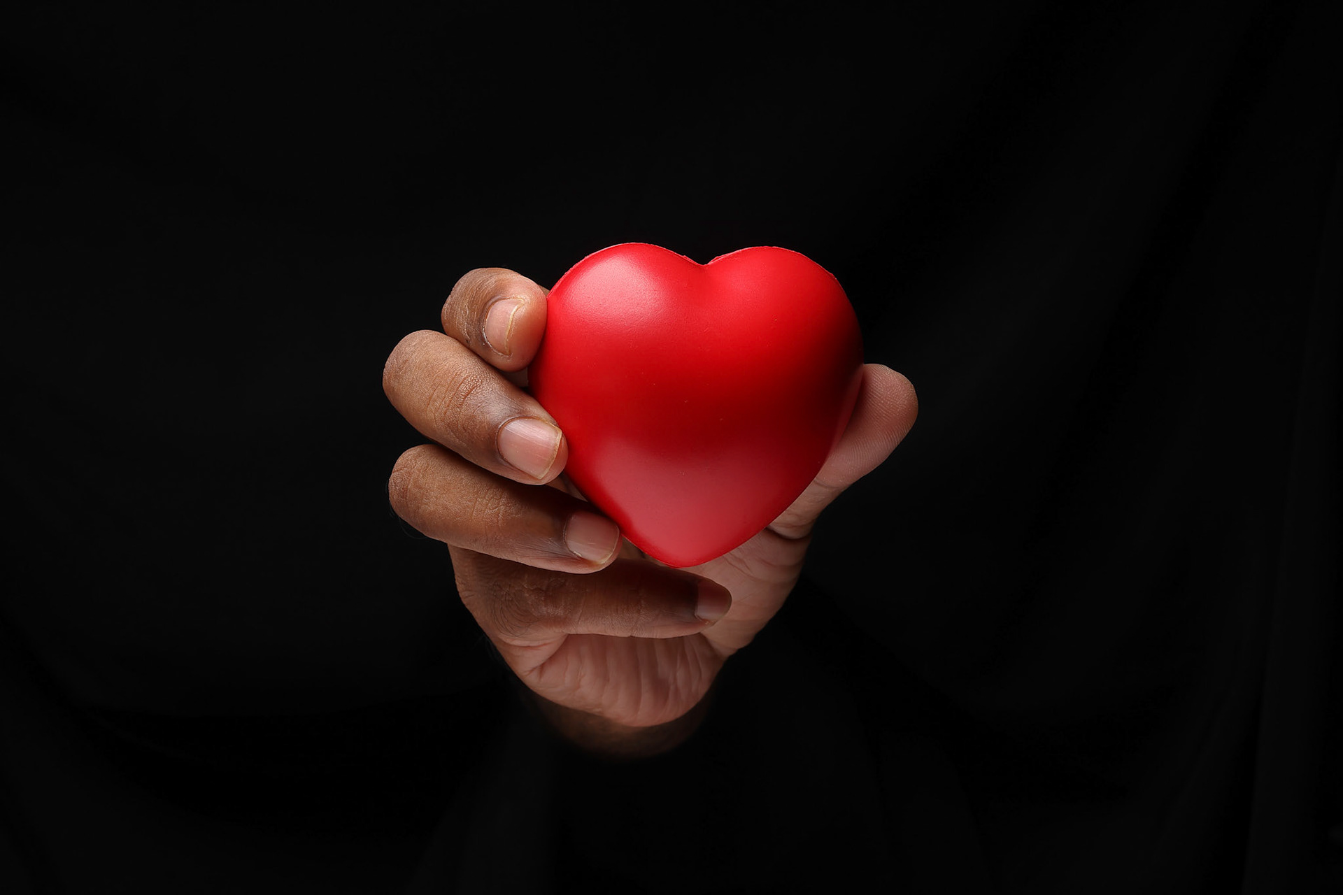 Asian male dark skinned single hand fist finger on black background holding red rubber hart love shape