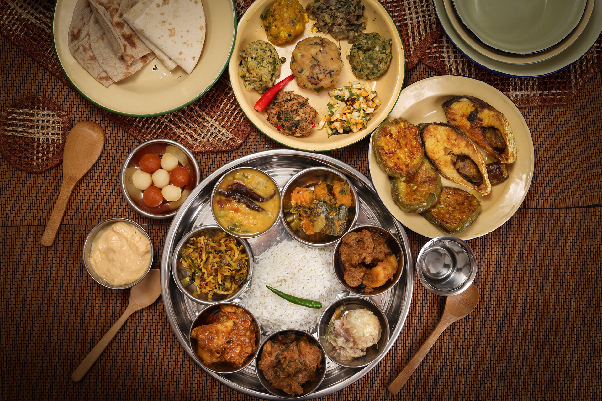 Bengali style thali spread verity cuisine hilsa fish vegetable beef mutton egg curry fry vorta mashed chicken liver sweet yogurt side dish served on rustic metal tin stainless steel plate small bowls