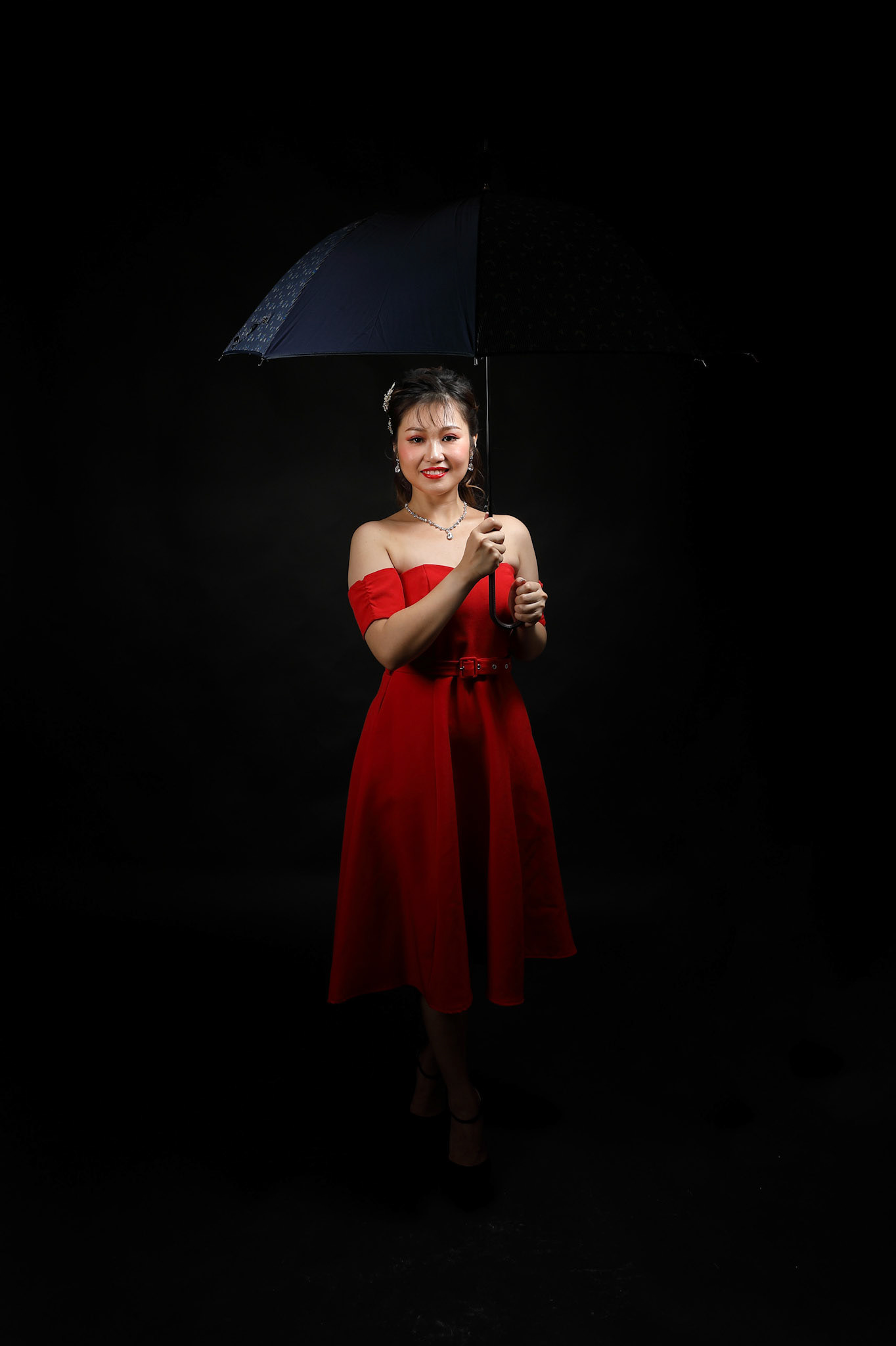 Asian woman in modern red dress under umbrella on black background