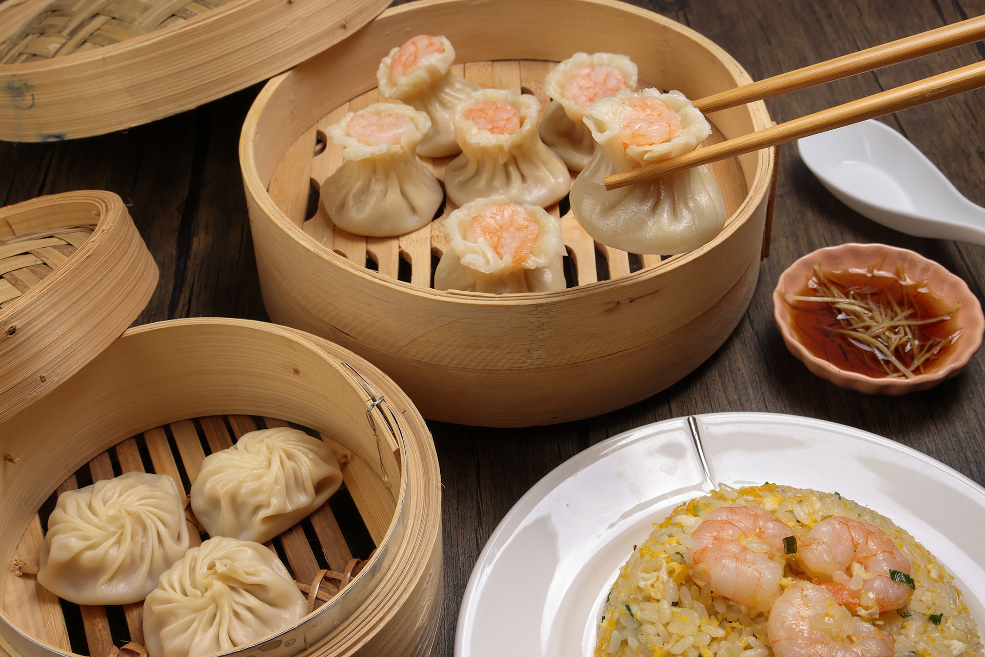 Prawn shrimp shaomai pickup by chopsticks Xiao long bao dim sum dumpling chicken prawn fish seafood vegetable in bamboo steamer fried rice on plate sauce soup spoon over rustic background