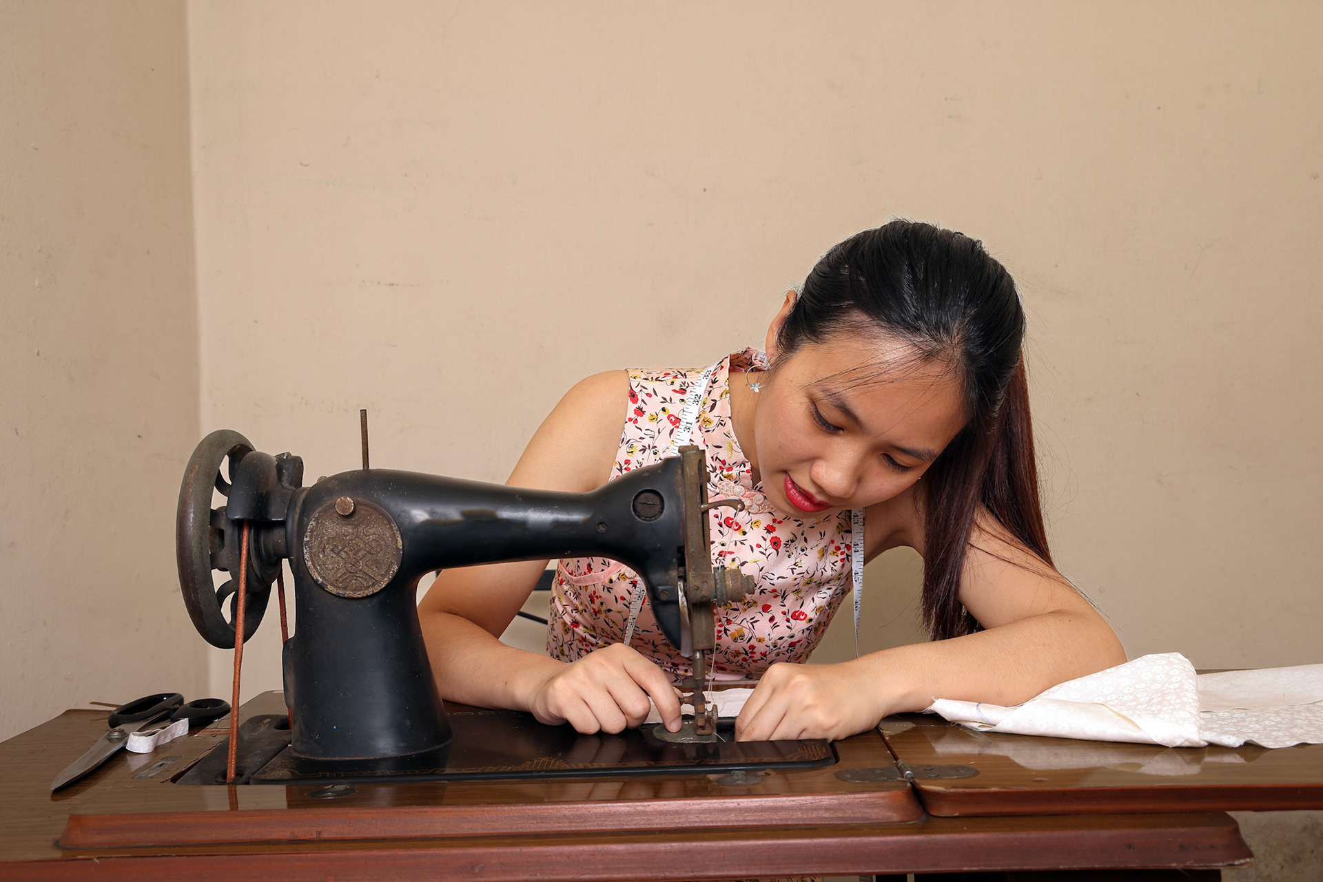 Young Asian woman using tailoring cloth fabric on a retro vintage old sewing machine