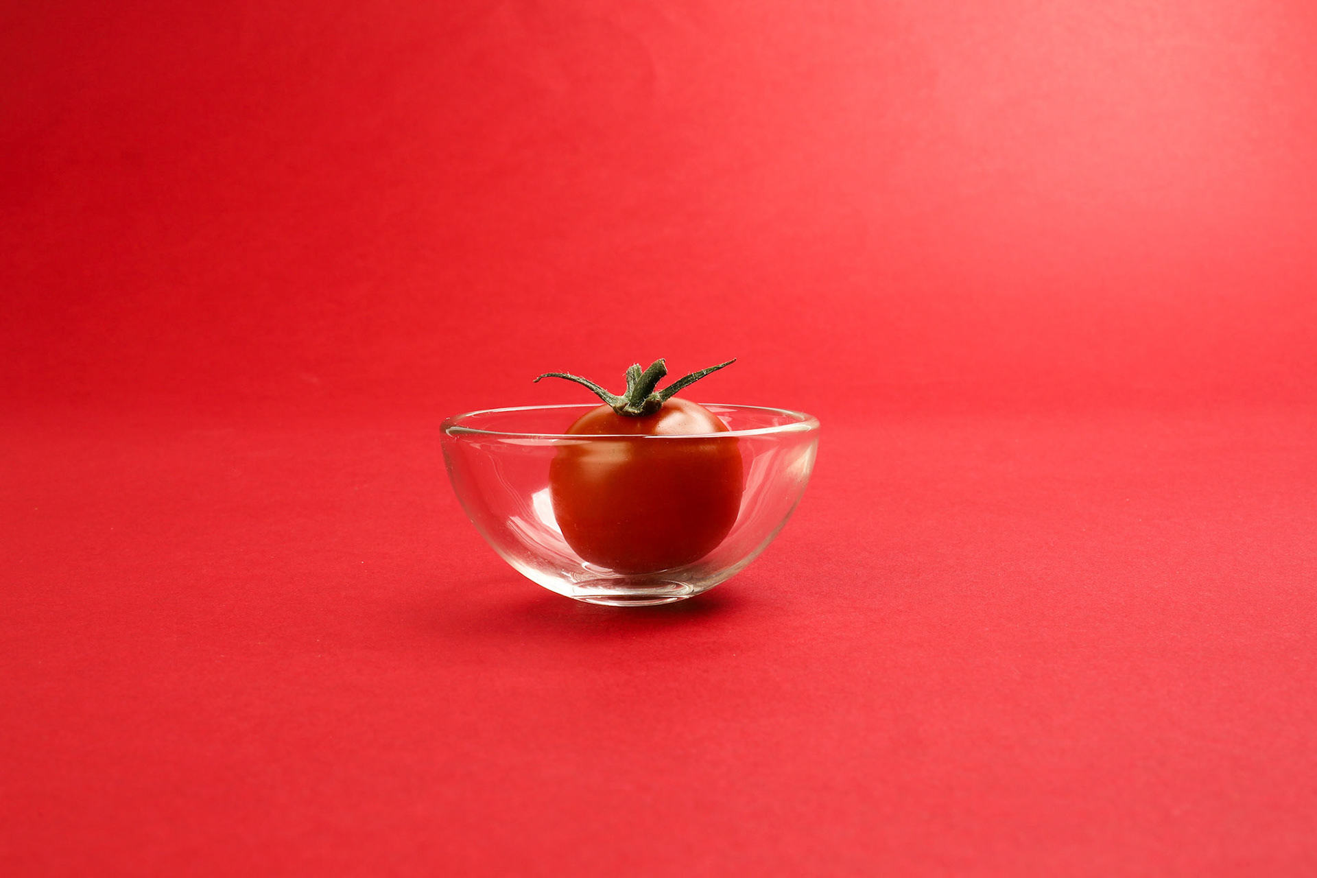 Red ripe cherry tomato with stem on red paper background copy text space mini glass bowl
